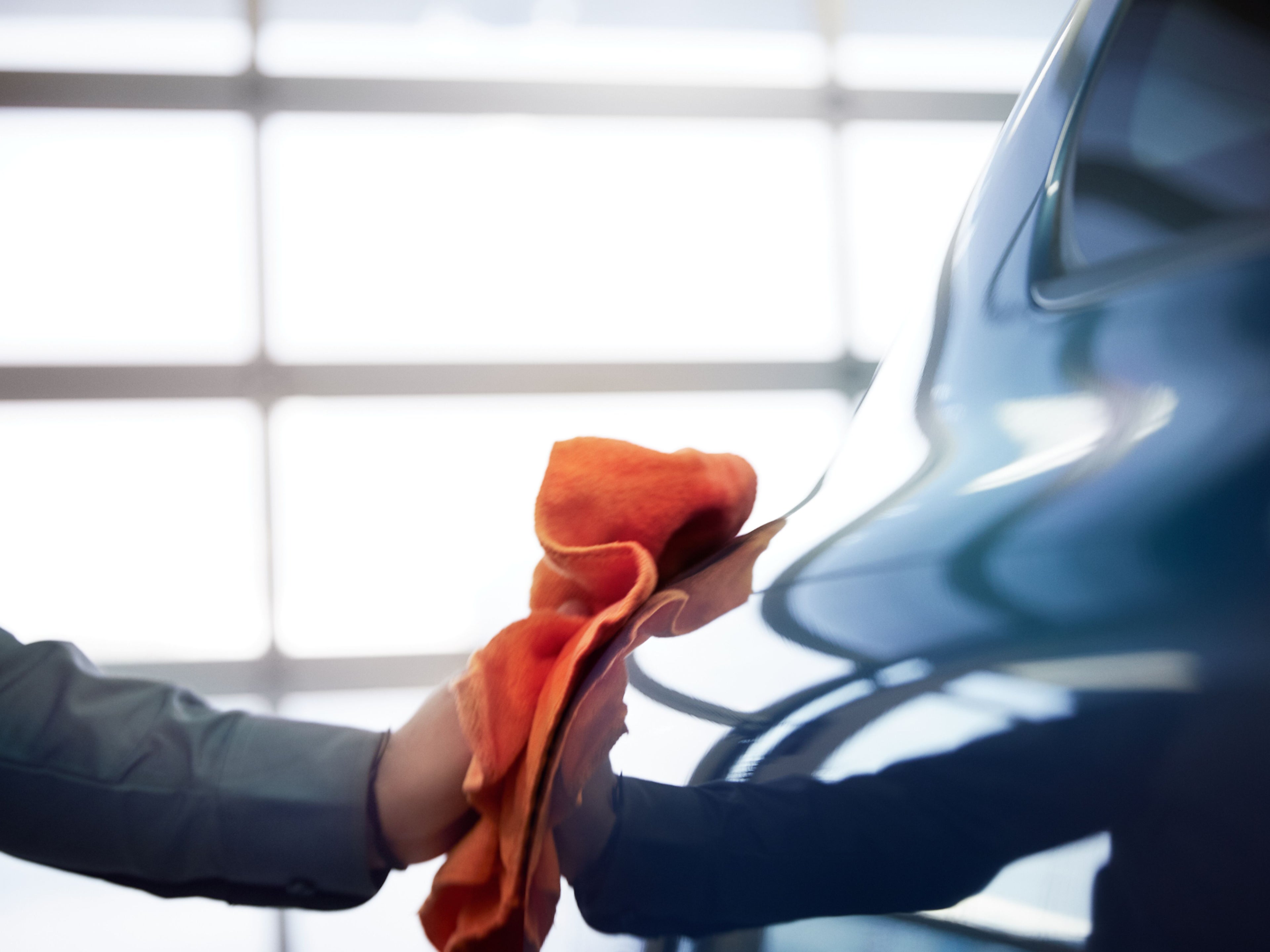 Eine Person poliert mit einem Lappen die Seite eines Fahrzeugs.