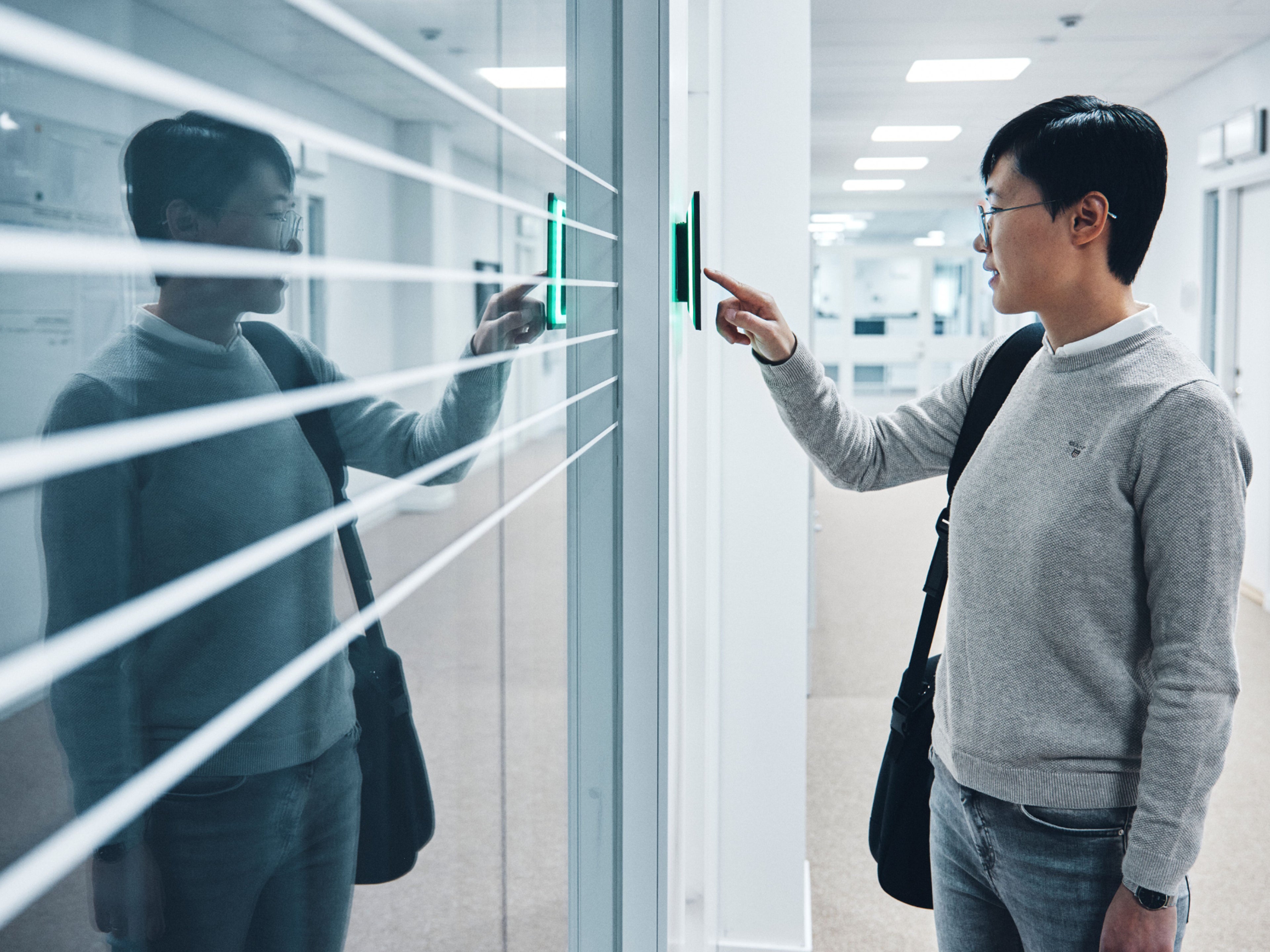 Eine Person steht vor einer Glaswand und tippt auf ein Display.