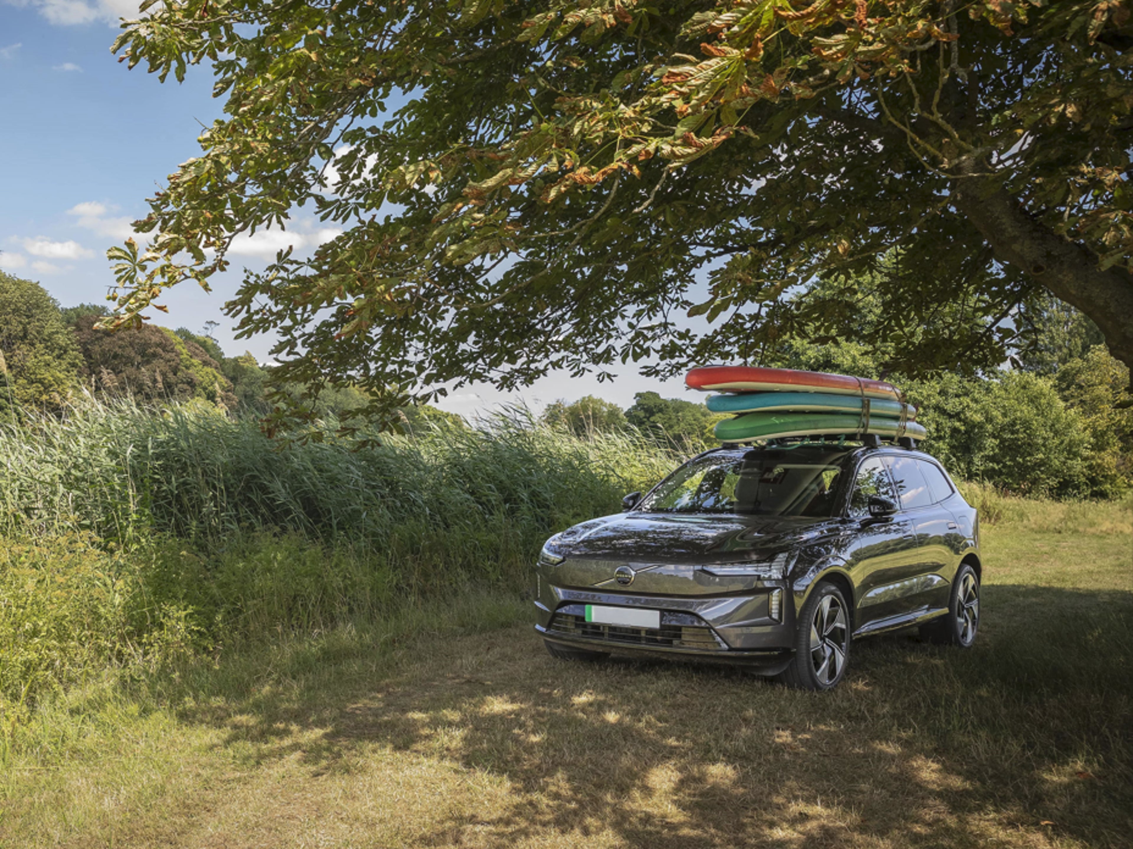 Volvo EX90 parked under canopy of green leafy trees in the countryside
