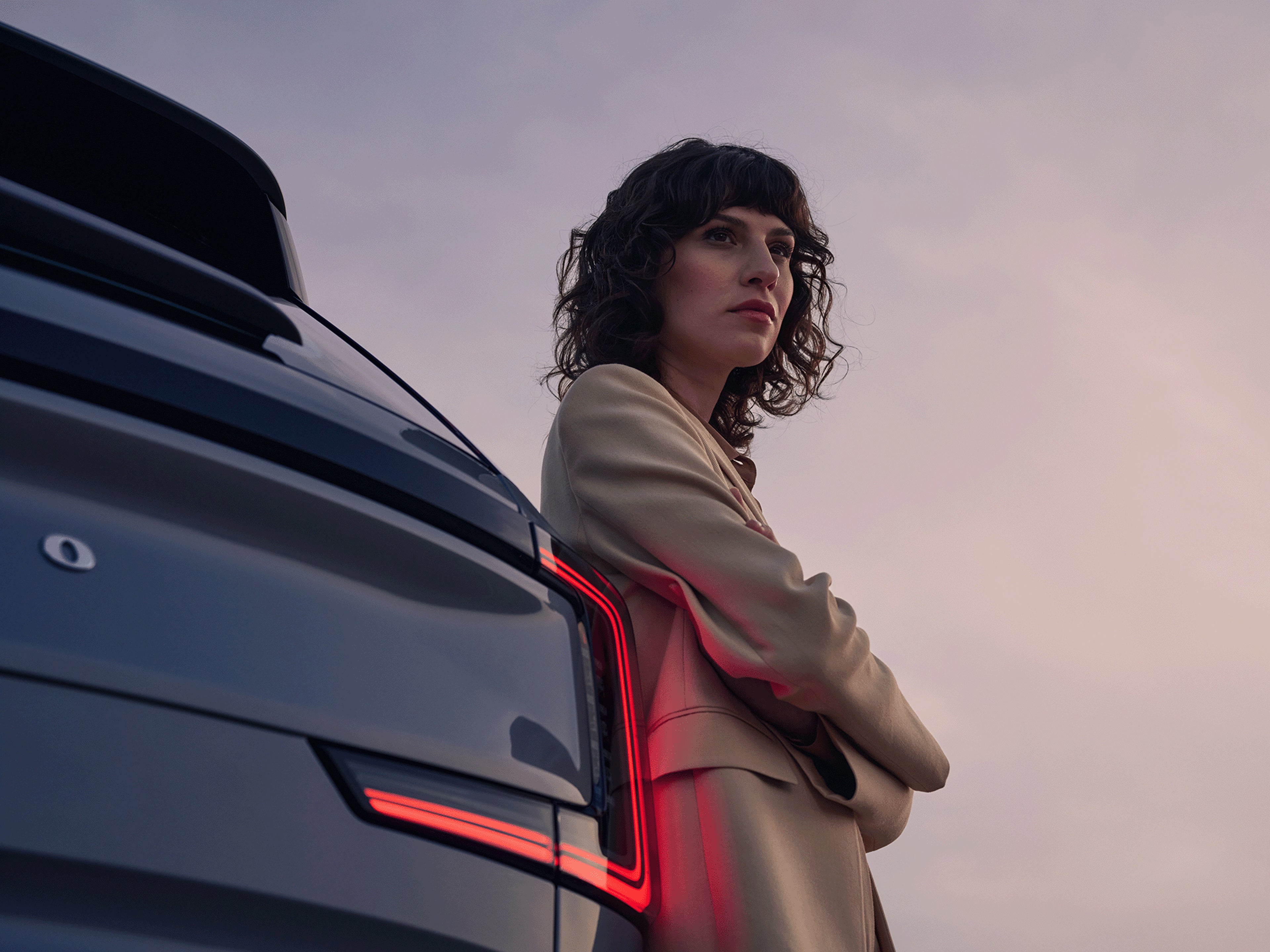 Eine Frau lehnt am Heck eines Volvo EX90.