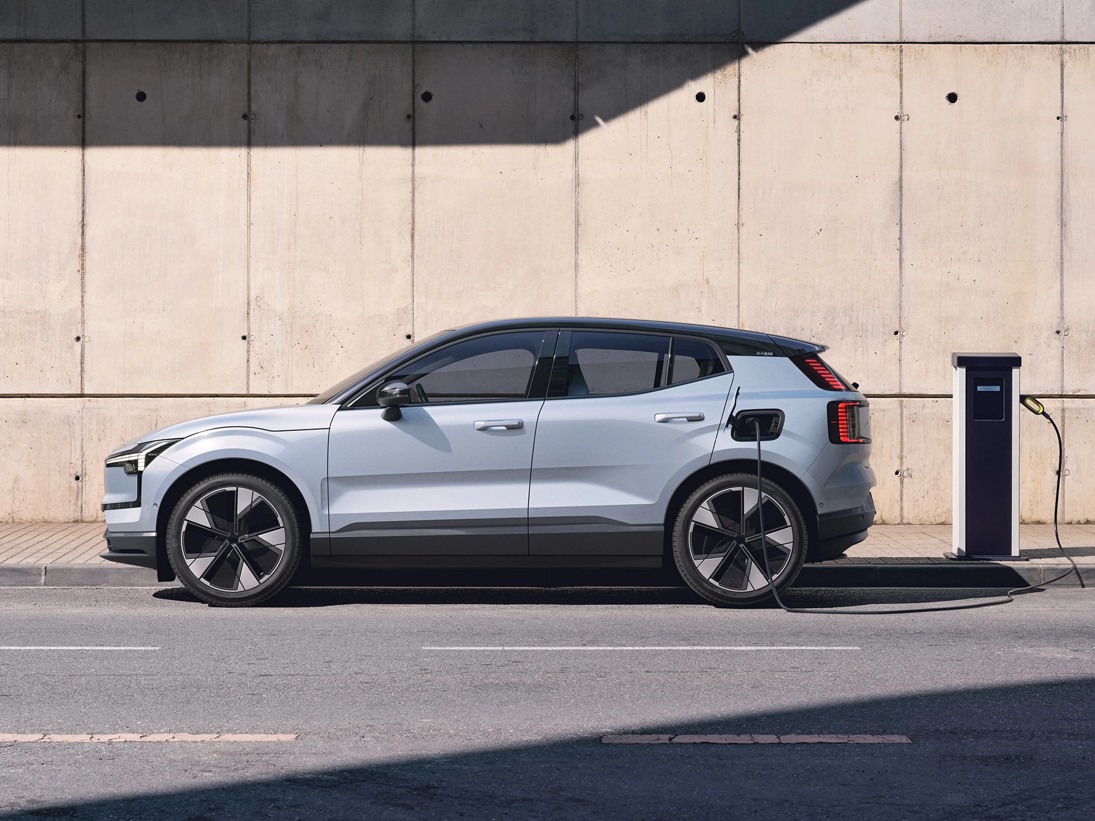 Cloud blue -värinen Volvo EX30 täyssähköinen katumaasturi kytkettynä lataukseen kadun reunalla sijaitsevalla latausasemalla.