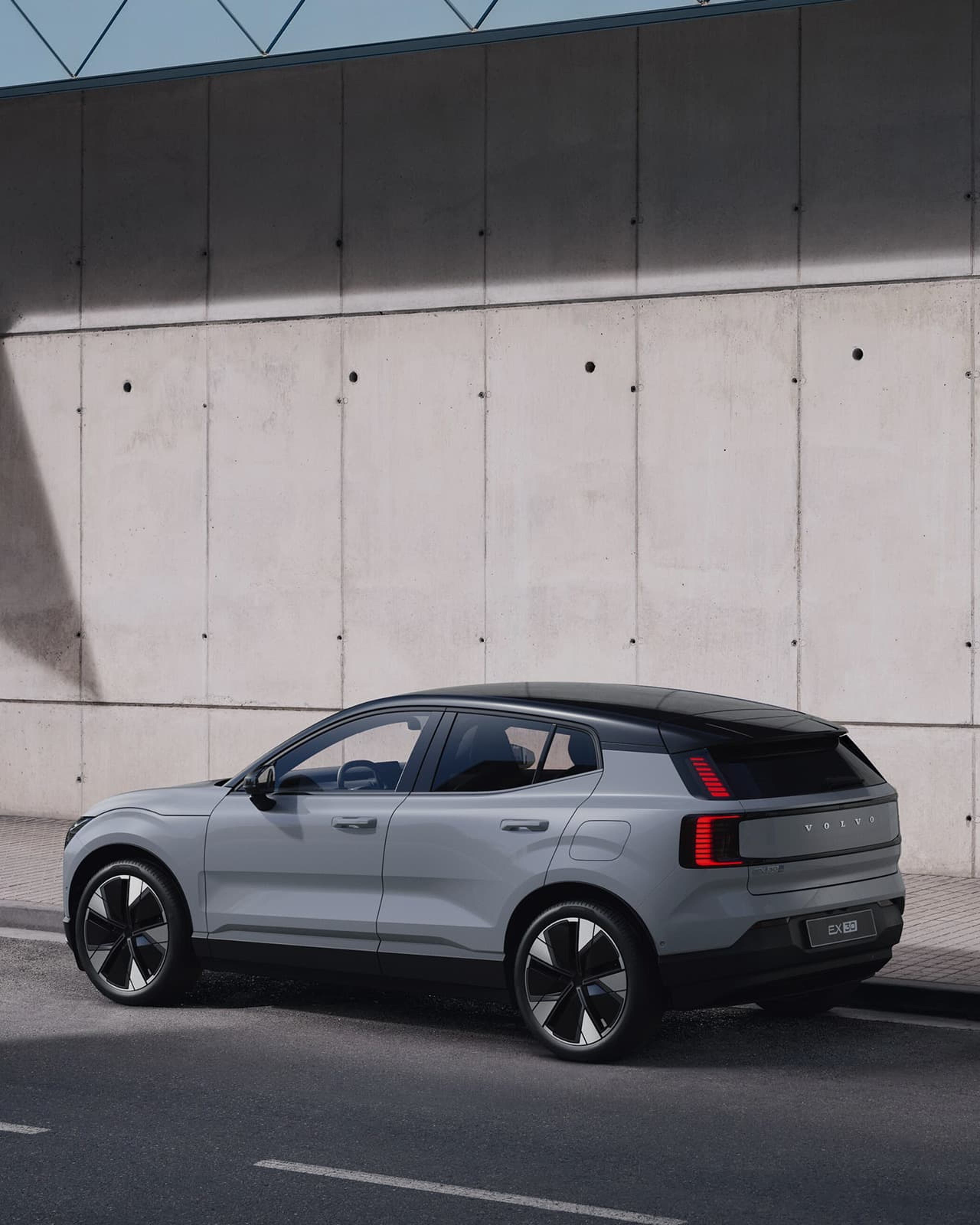 Une Volvo EX30 grise avec un toit noir est garée devant un mur en béton.