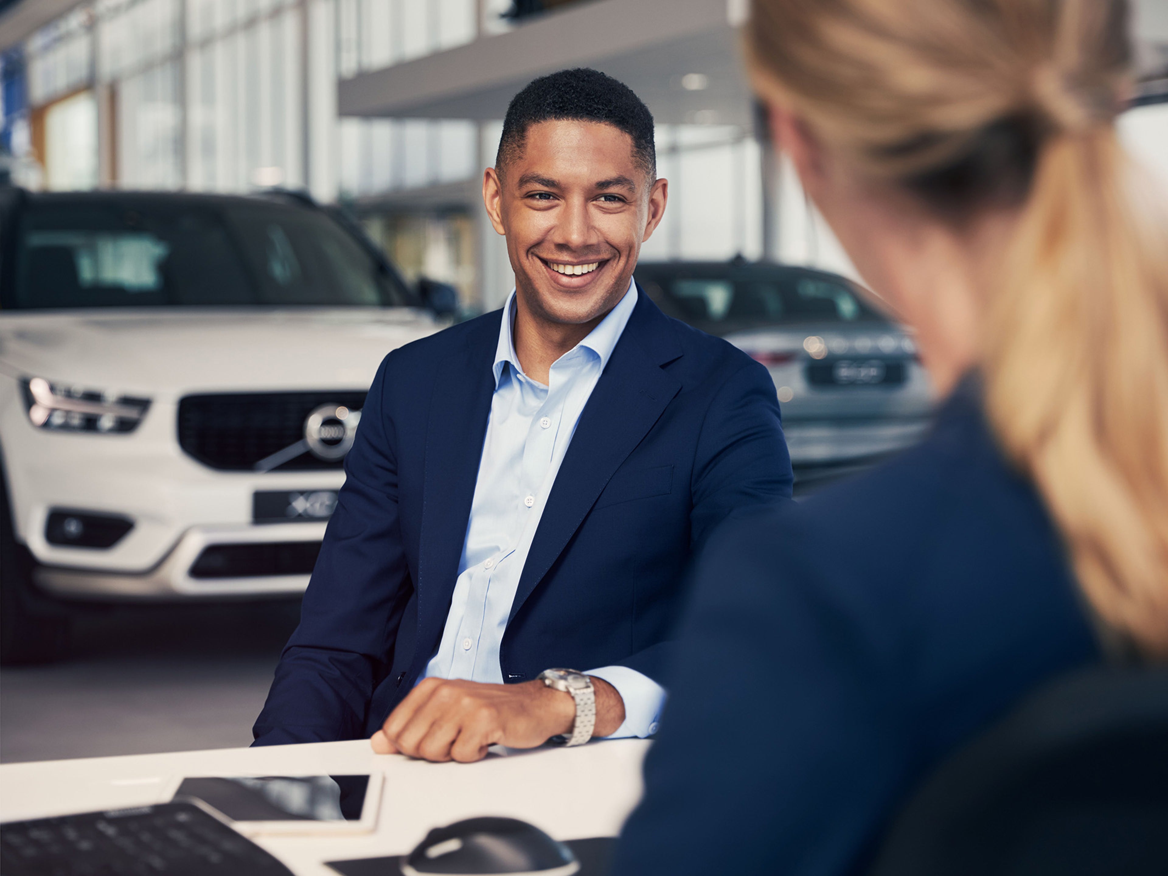 Cliente num concessionário volvo, sorridente, com dois volvo em segundo plano