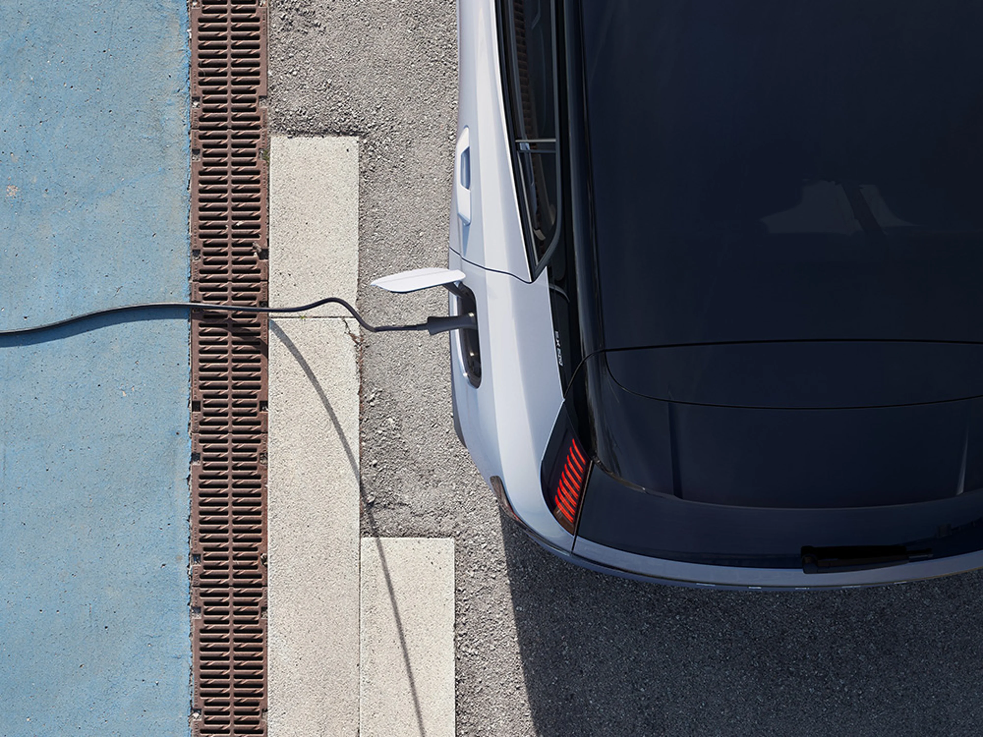 Vue aérienne d'une Volvo EX30 blanche à toit noir en cours de recharge à une borne de recharge publique.