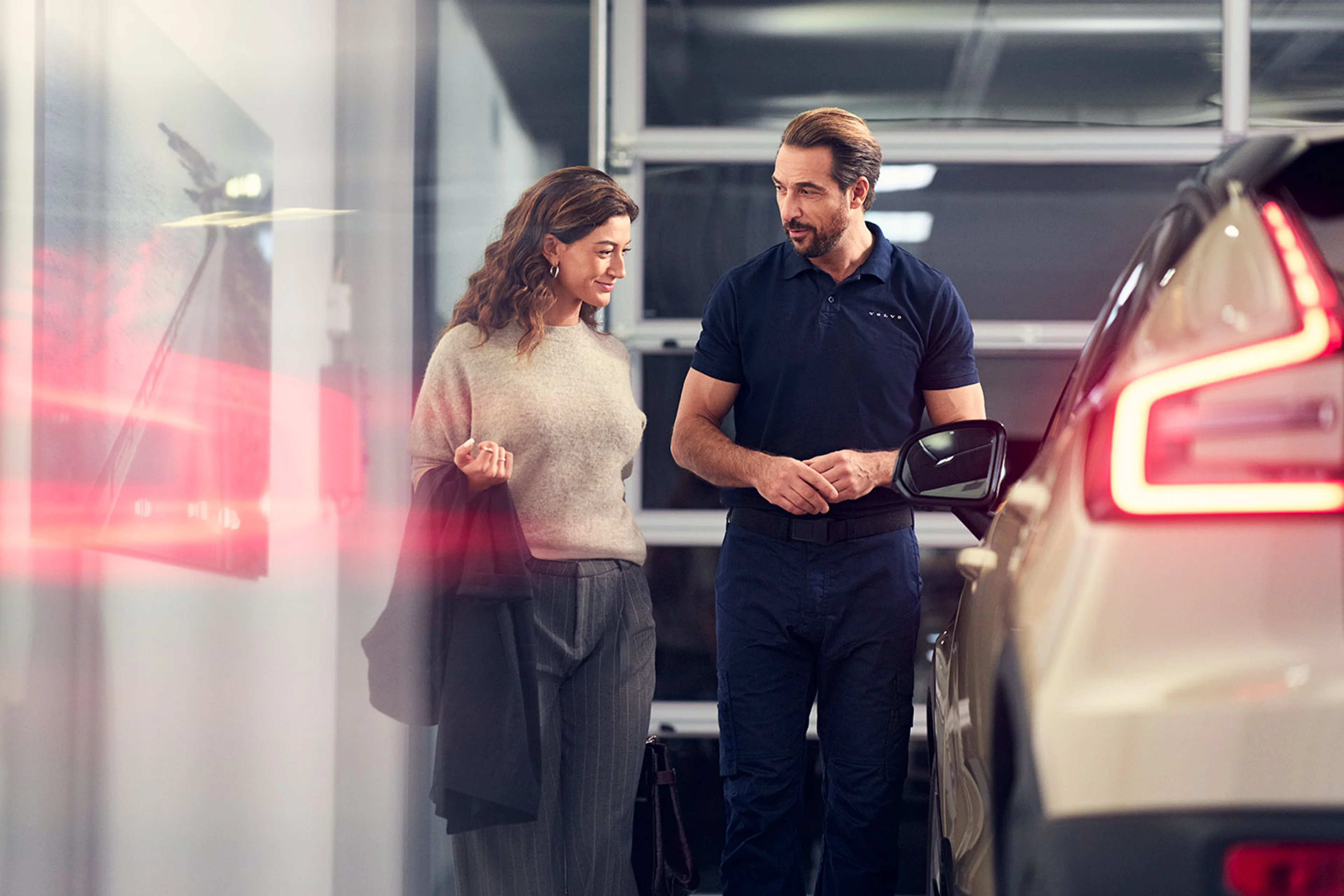 En mandlig service tekniker informerer en kvindelig kunde om hvilket arbejde der er lavet på hendes Volvo bil, set forfra i frøperspektiv i et showroom miljø.
