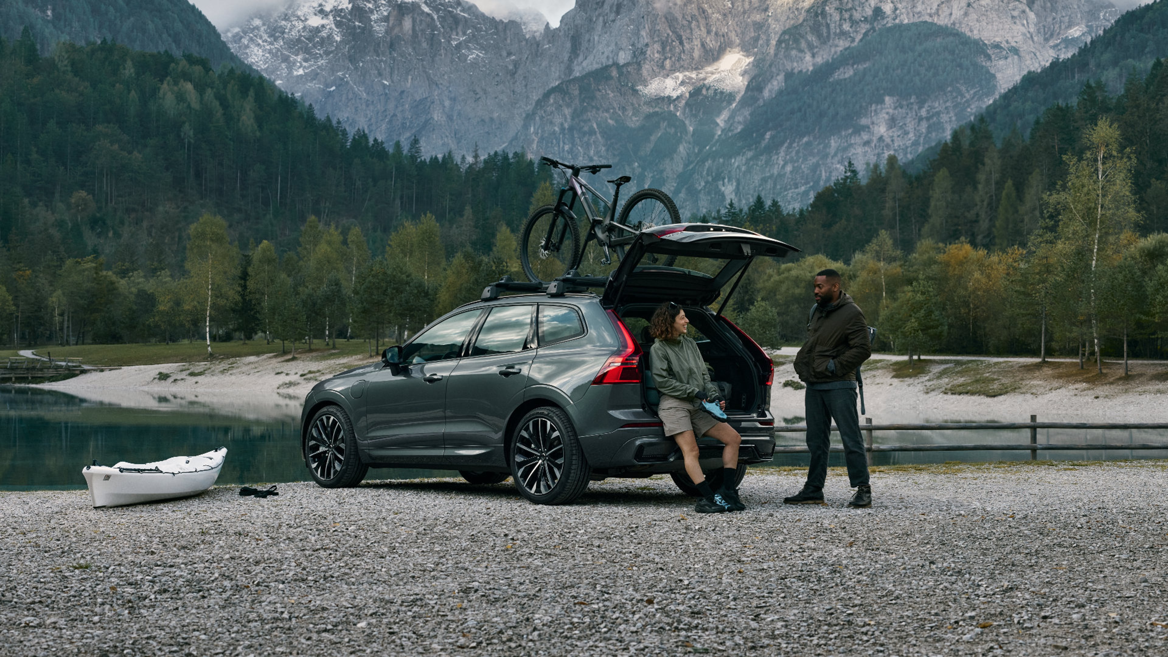 Eine Frau sitzt in dem geöffneten Kofferraum eines dunkelgrauen Volvo XC60 SUV und unterhält sich mit einem Mann.