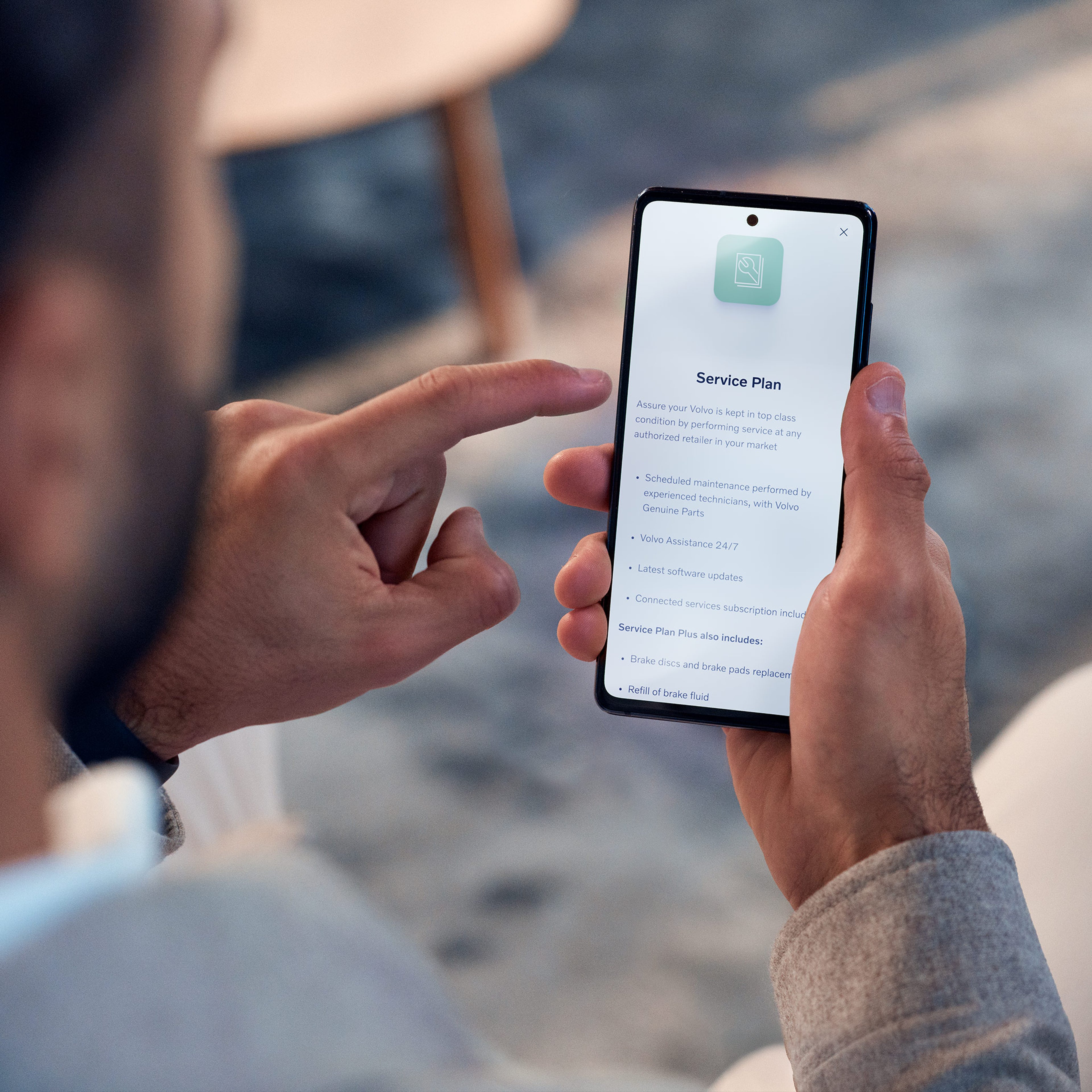 Mies lukee kädessään olevan puhelimen näytöltä lisätietoa Volvo Huoltosopimuksesta Volvo Car -sovelluksessa .