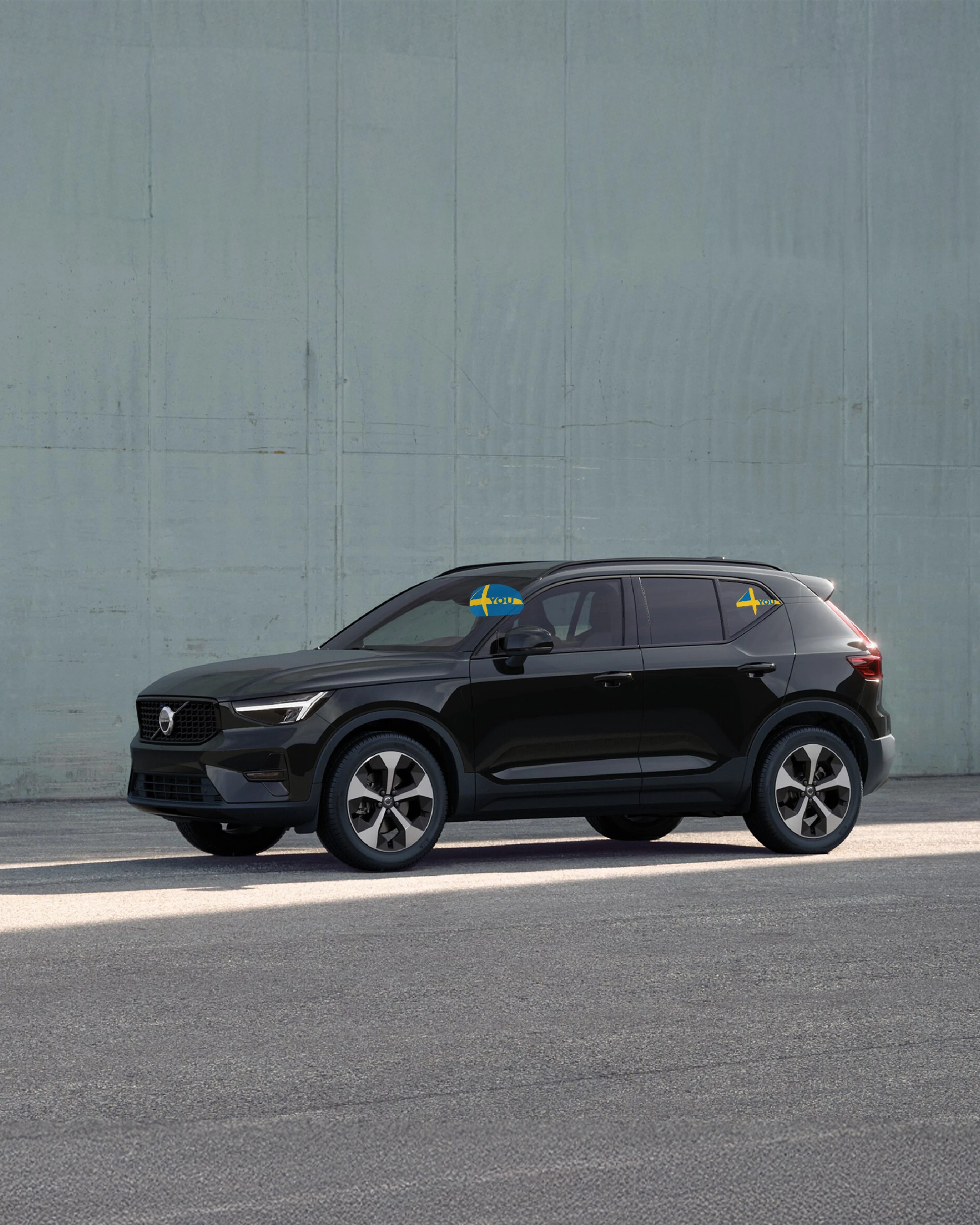 Ein schwarzer Volvo XC40 steht seitlich in einem Outdoor Umfeld vor einer grünen Wand.