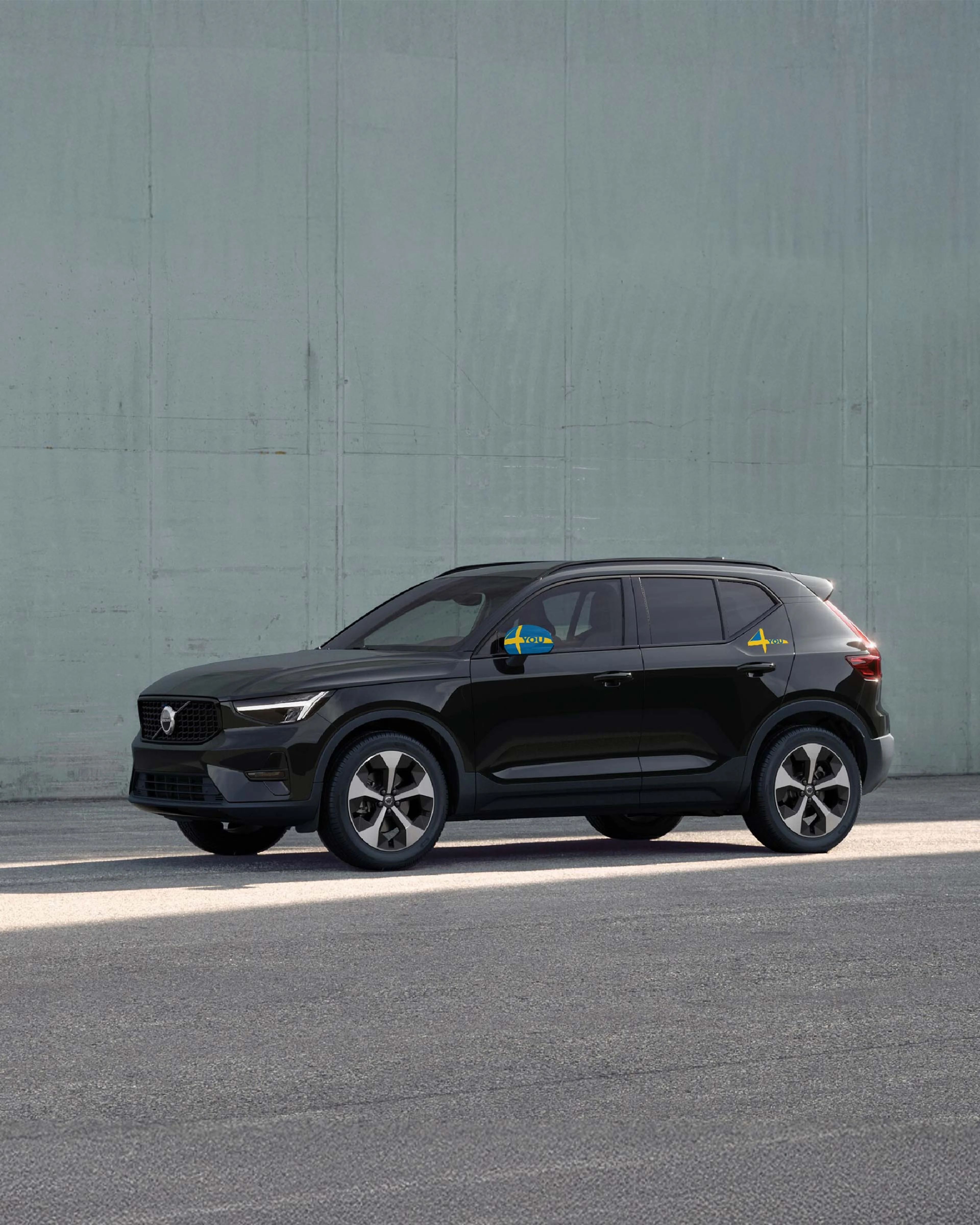 Ein schwarzer Volvo XC40 steht seitlich in einem Outdoor Umfeld vor einer grünen Wand.
