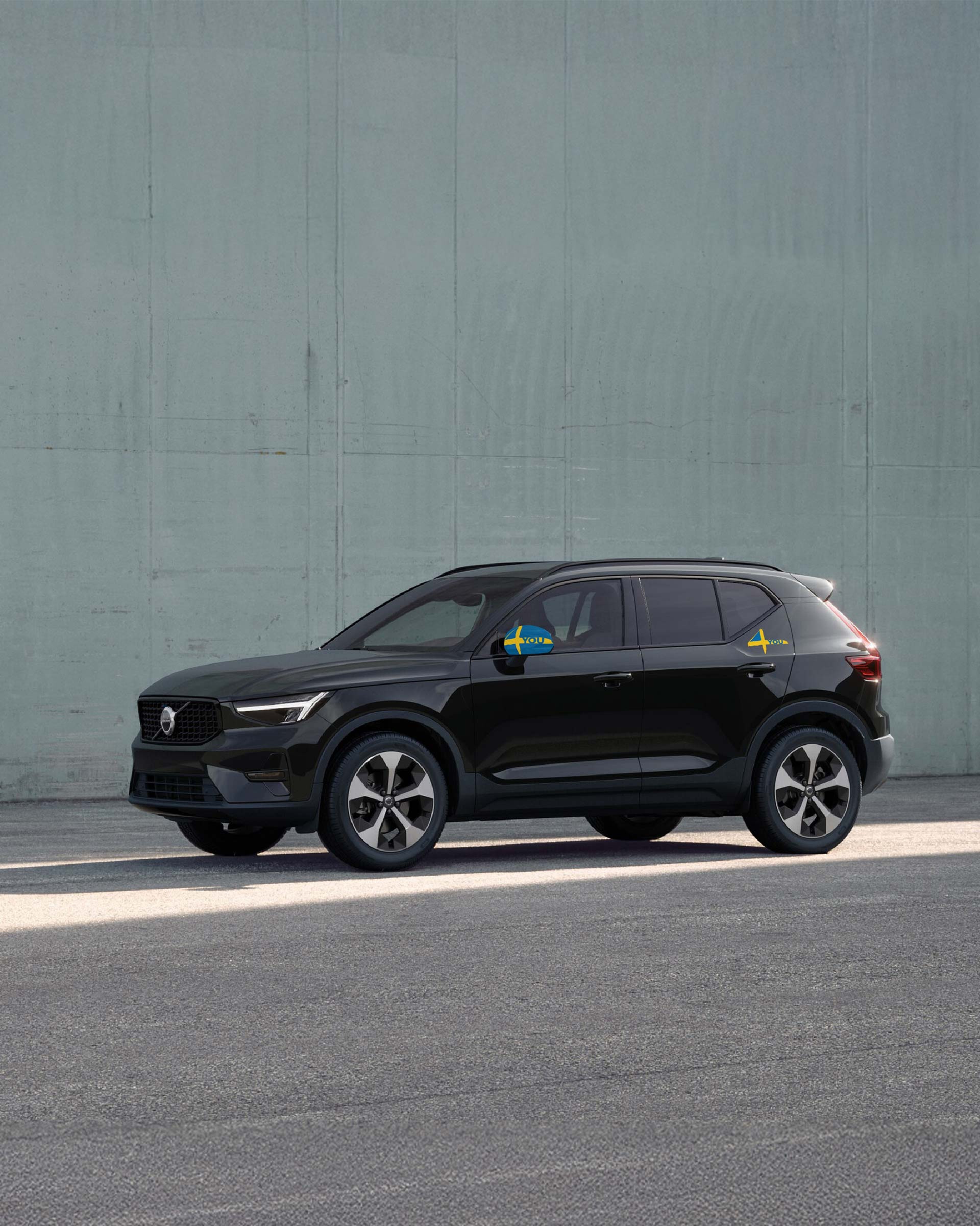 Ein schwarzer Volvo XC40 steht seitlich in einem Outdoor Umfeld vor einer grünen Wand.