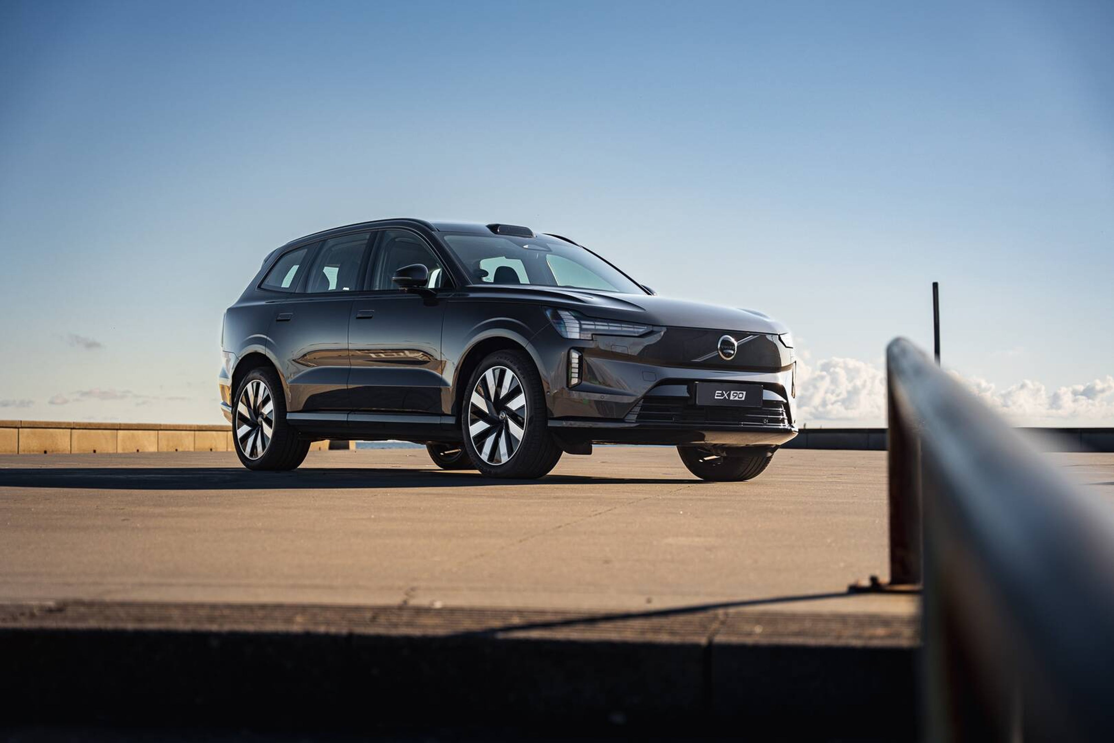 Elegant sort Volvo SUV på en tagterrasse-parkeringsplads under en klar blå himmel, som symboliserer modernitet og elegance, med sollys der reflekteres i dens polerede overflade.