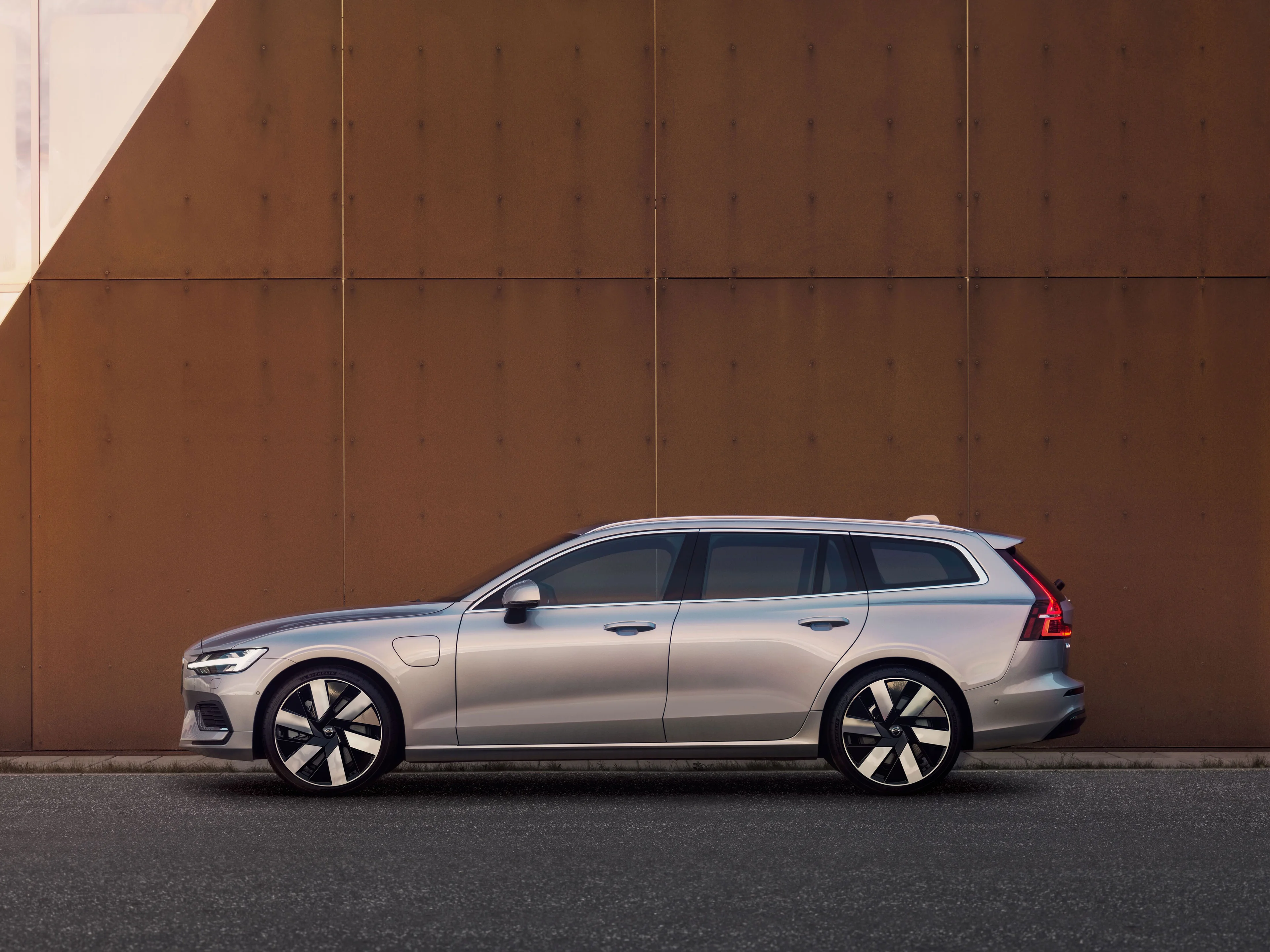 Ein silberner Volvo V60 Kombi steht vor einer rostbraunen Wand.