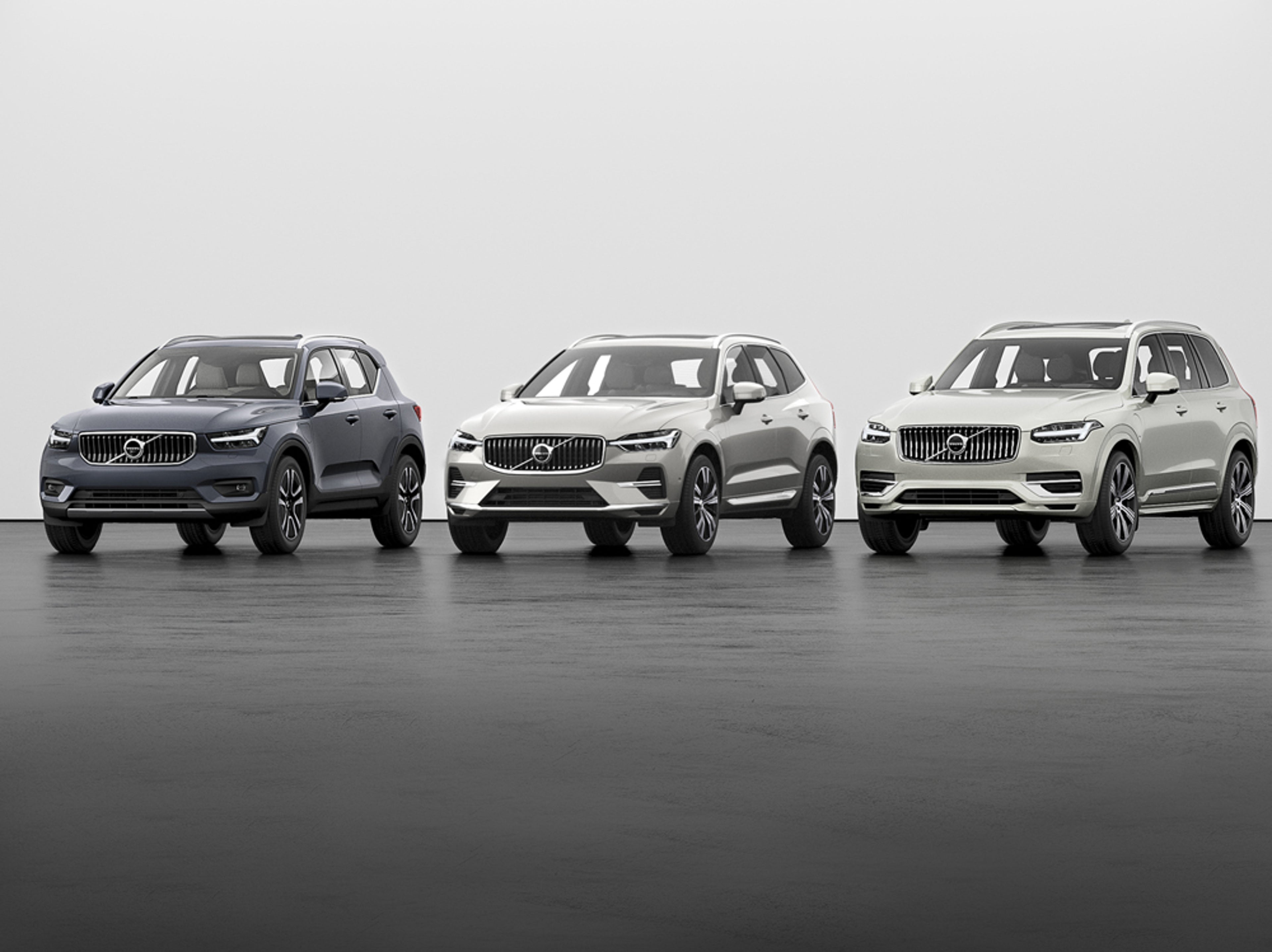Séð framan á gráan Volvo XC40, ljósgráan Volvo XC60 og hvítan Volvo XC90 snúa aðeins til vinstri í sýningarsal.