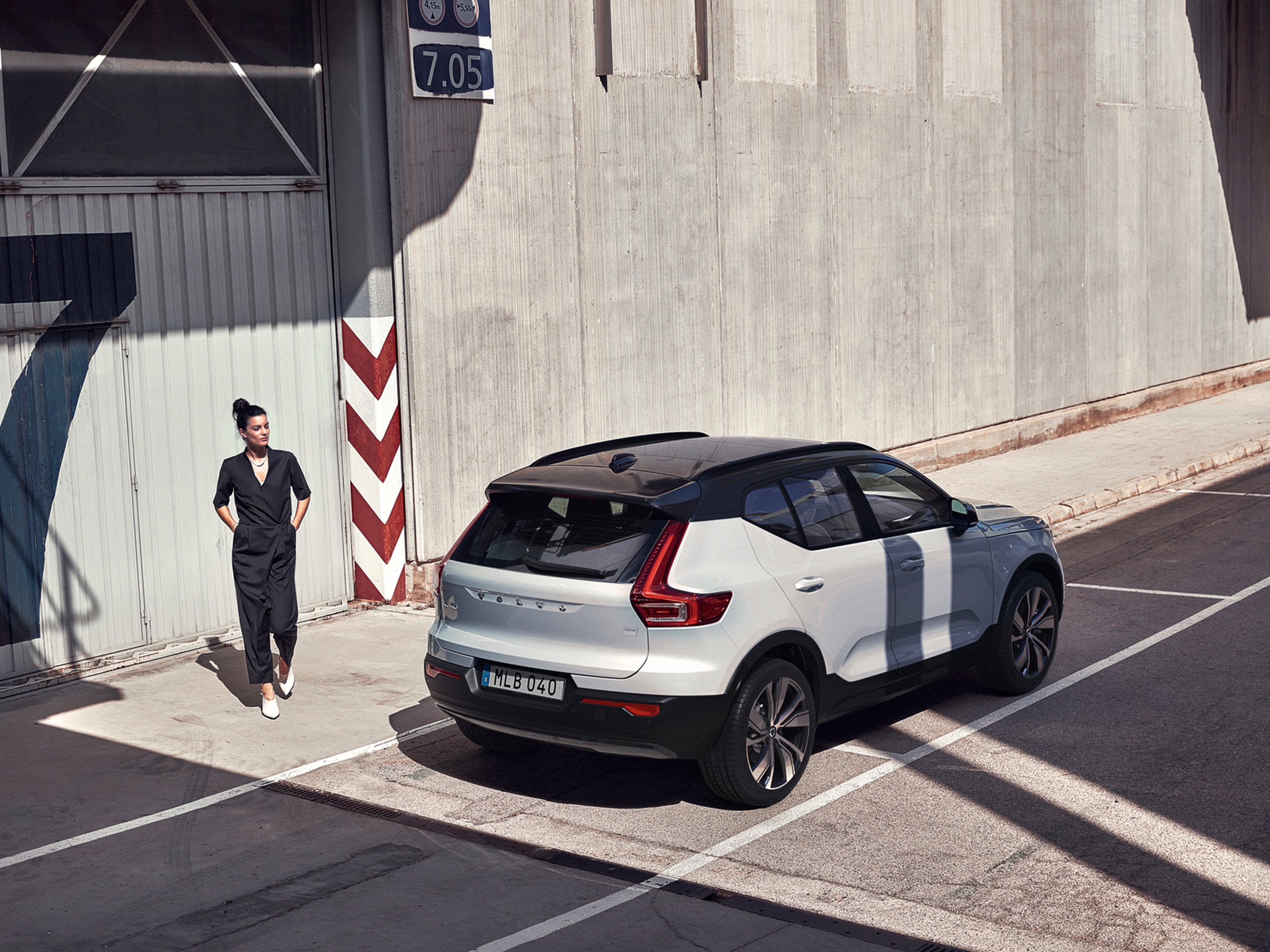 Una mujer parada sobre la banqueta son un Volvo XC40 blanco estacionado al frente.