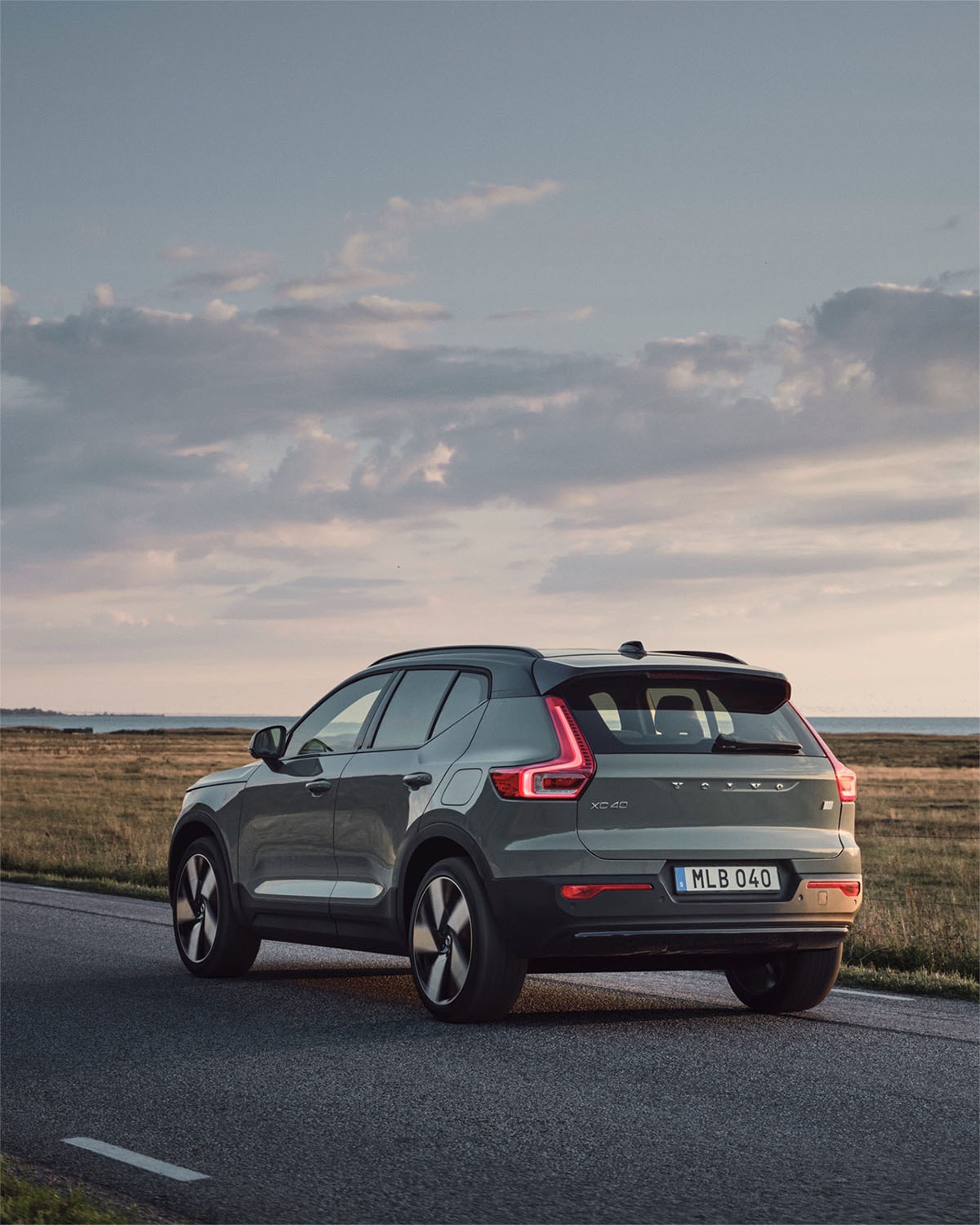 Volvo XC40 v zeleni barvi vozi po podeželski cesti ob sončnem zahodu.