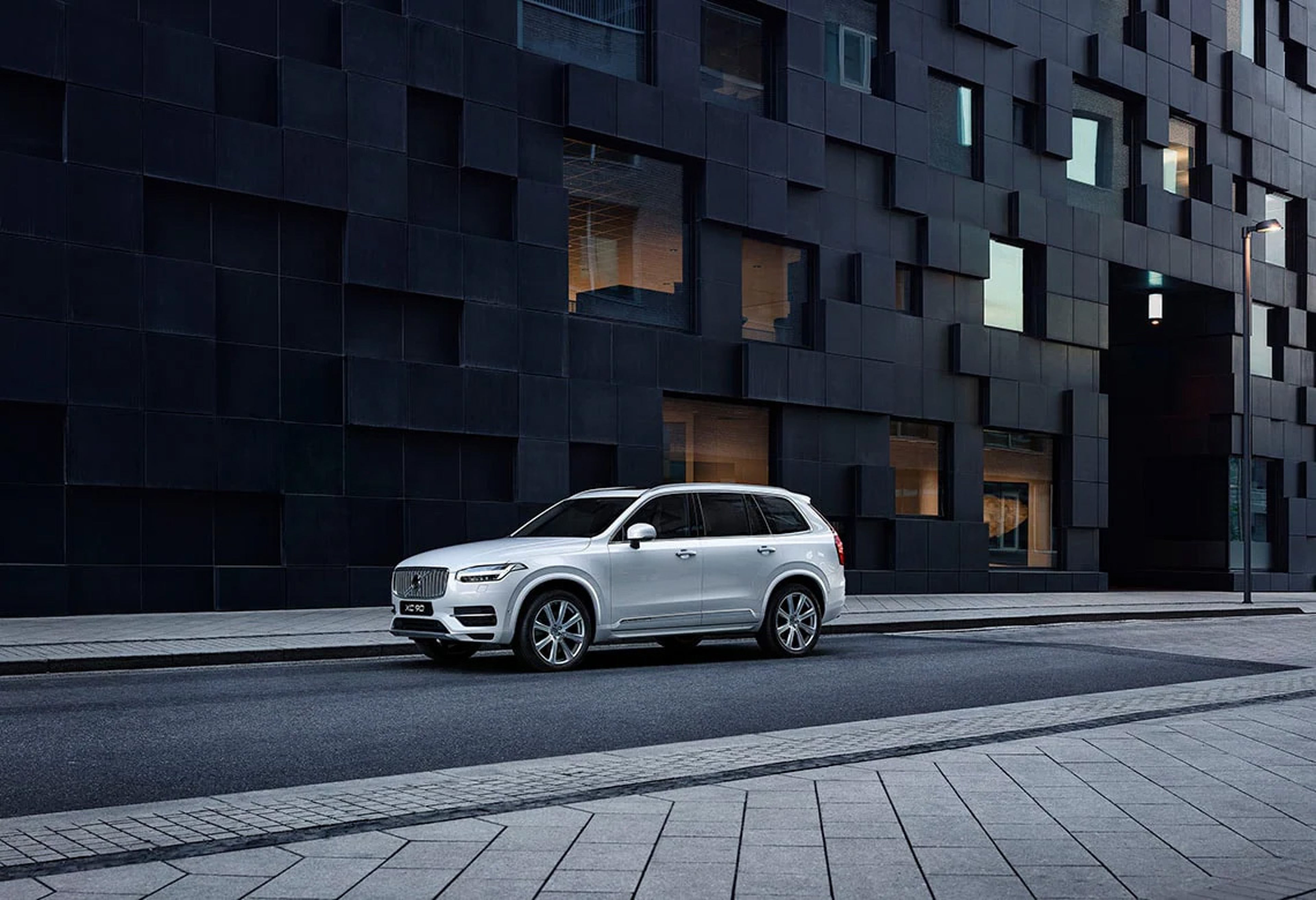 Ein silberner Volvo XC90 steht vor einem modernen, dunkel-verkleideten Wohngebäude.
