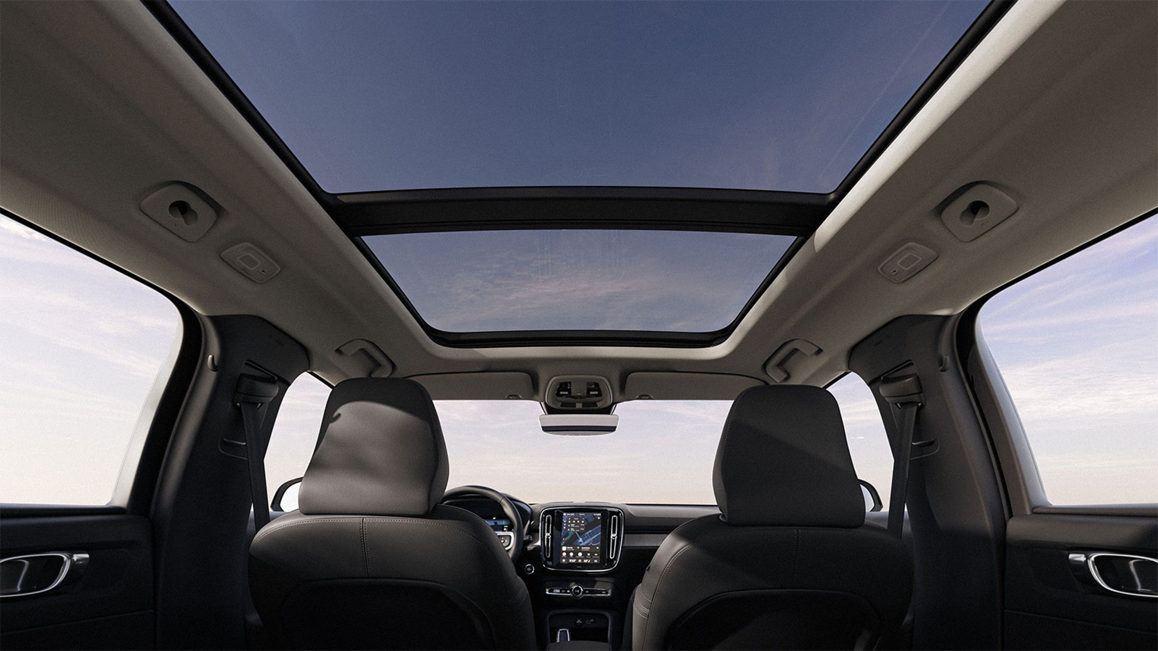 Vue intérieure d’une voiture avec toit panoramique, montrant les sièges avant et le tableau de bord