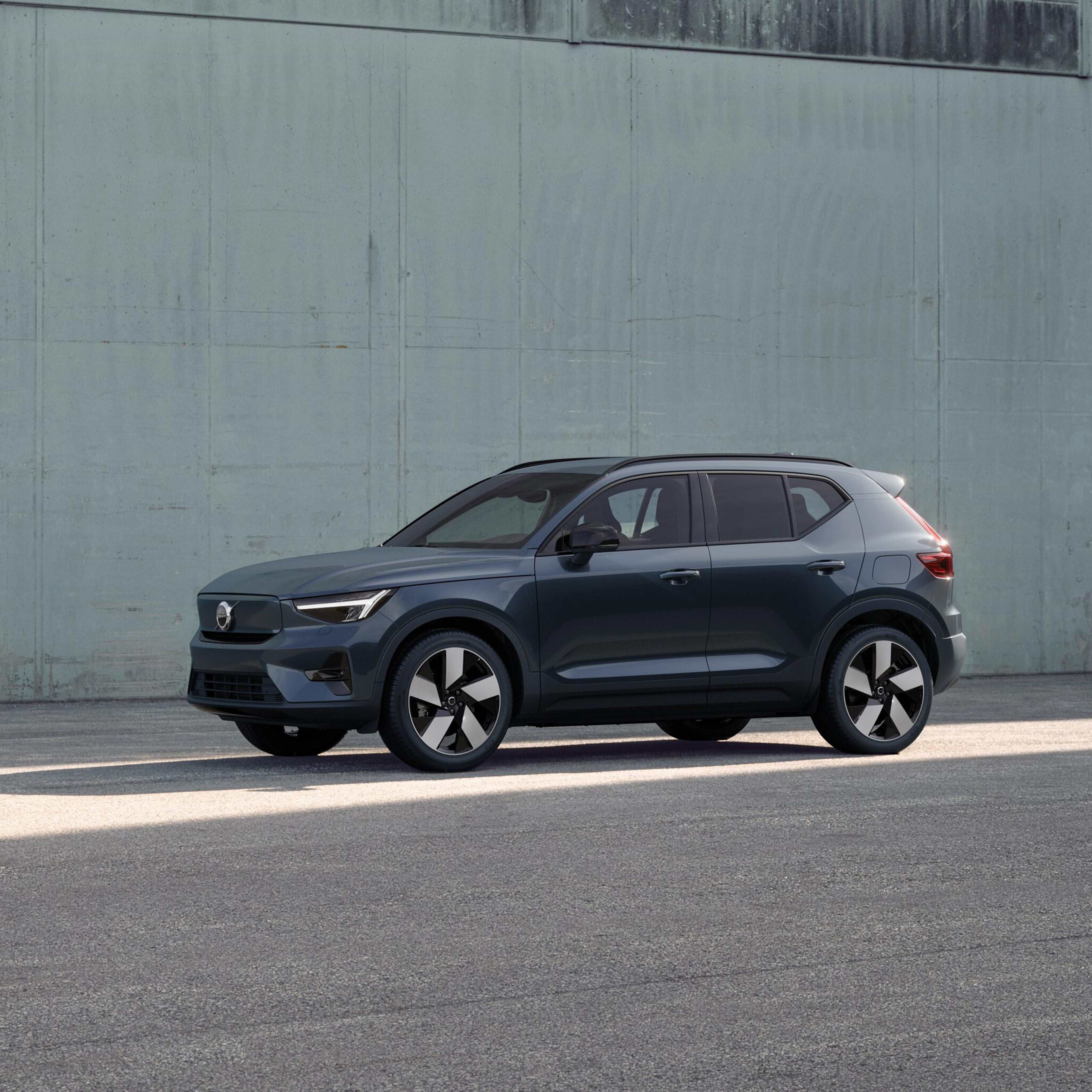 Forest lake -värinen Volvo EX40 Twin Plus täyssähköinen katumaasturi pysäköitynä vihertävän betoniseinän eteen.