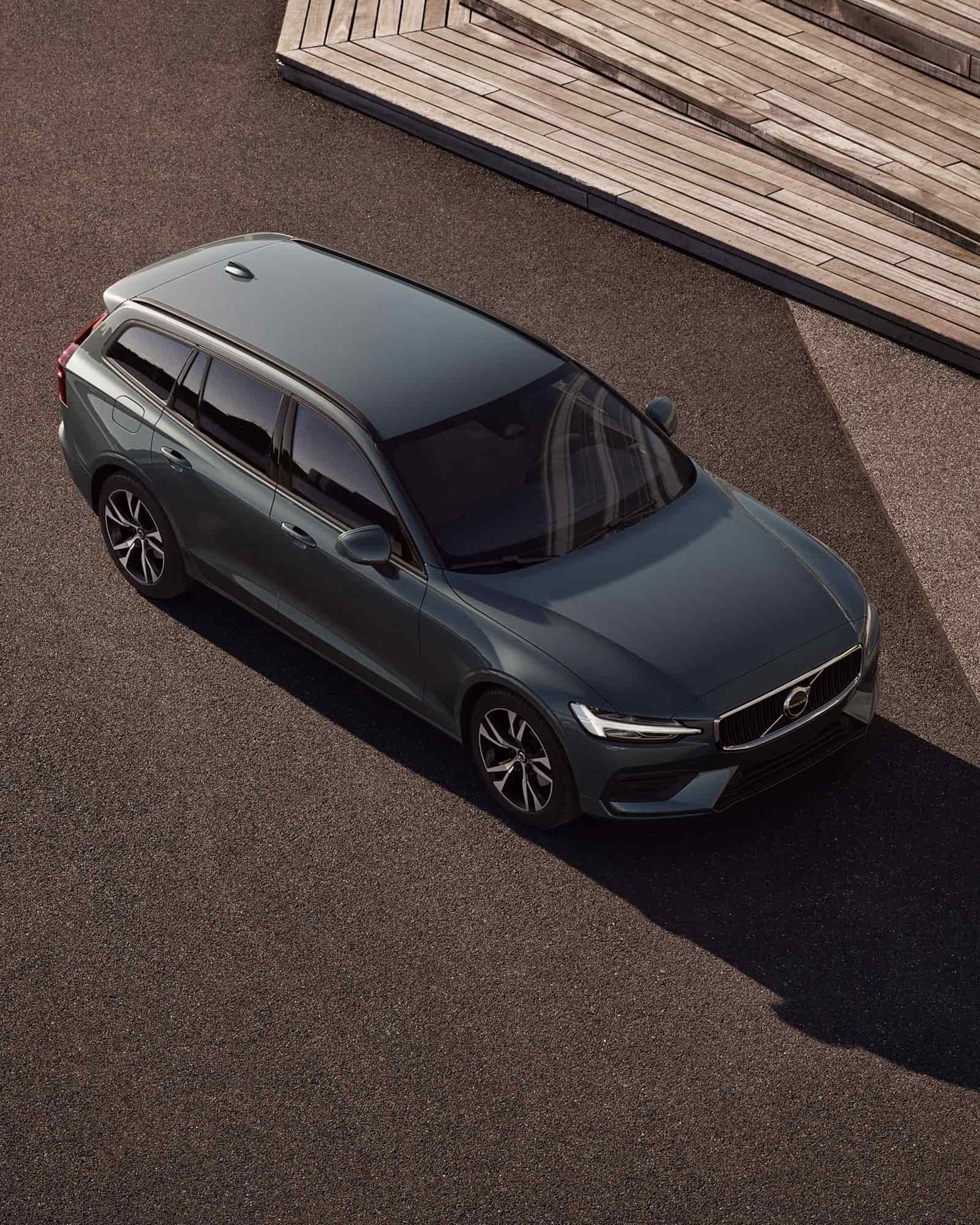 Vue aérienne d'une Volvo V60 verte foncée roulant sur un chemin de terre avec un escalier en bois sur le côté.