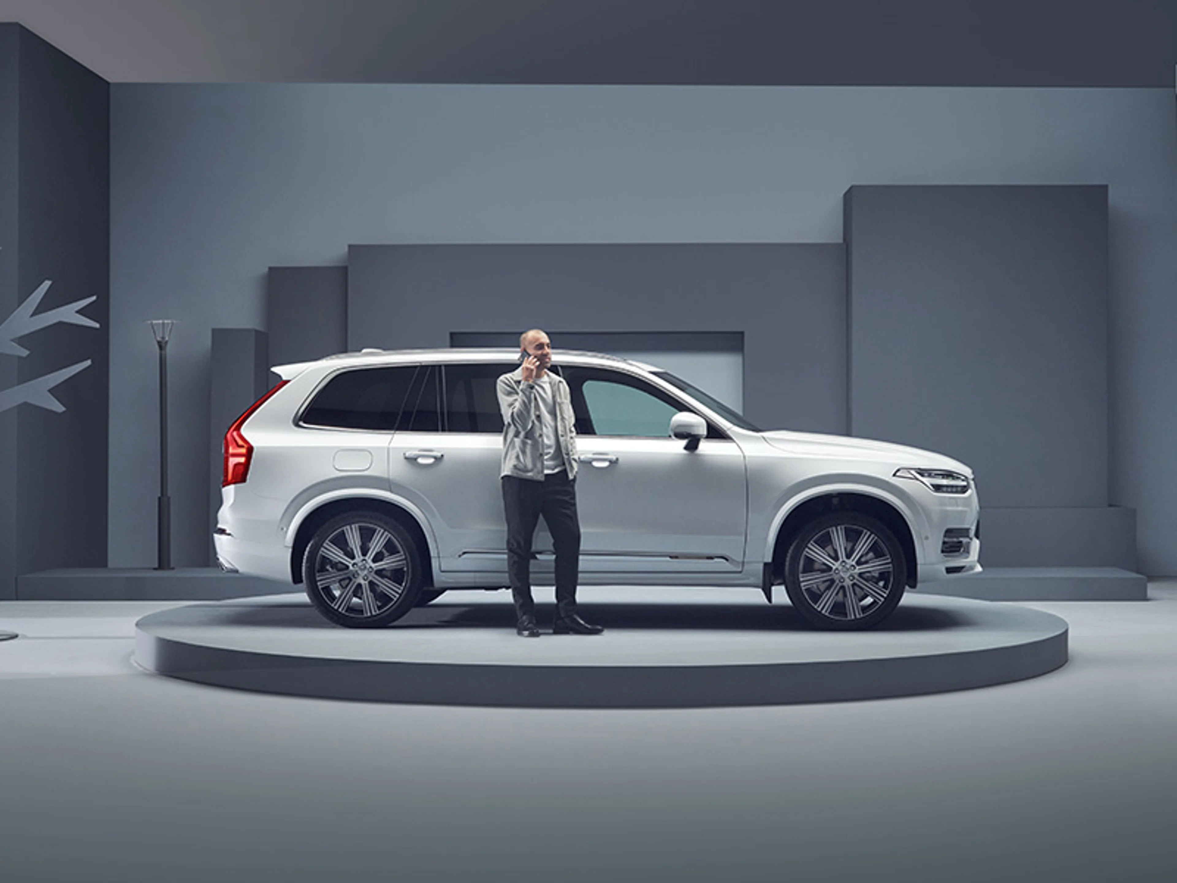 Homme qui utilise sa téléphone à coté d'une voiture XC90 blanche