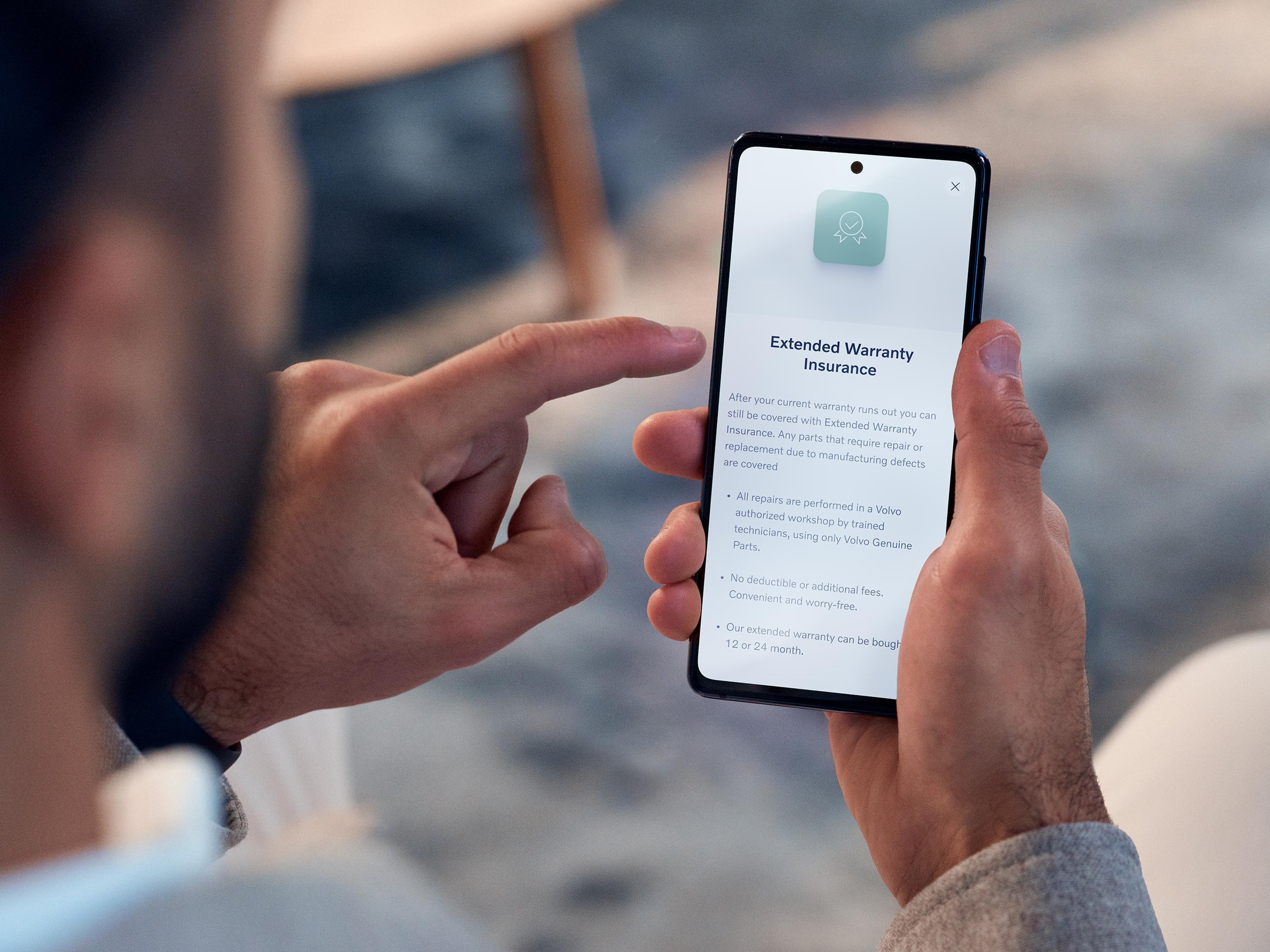 Miehen kädessä olevaan puhelimeen on avattu näkymä Volvo Extended Warranty Insurance sivulle.
