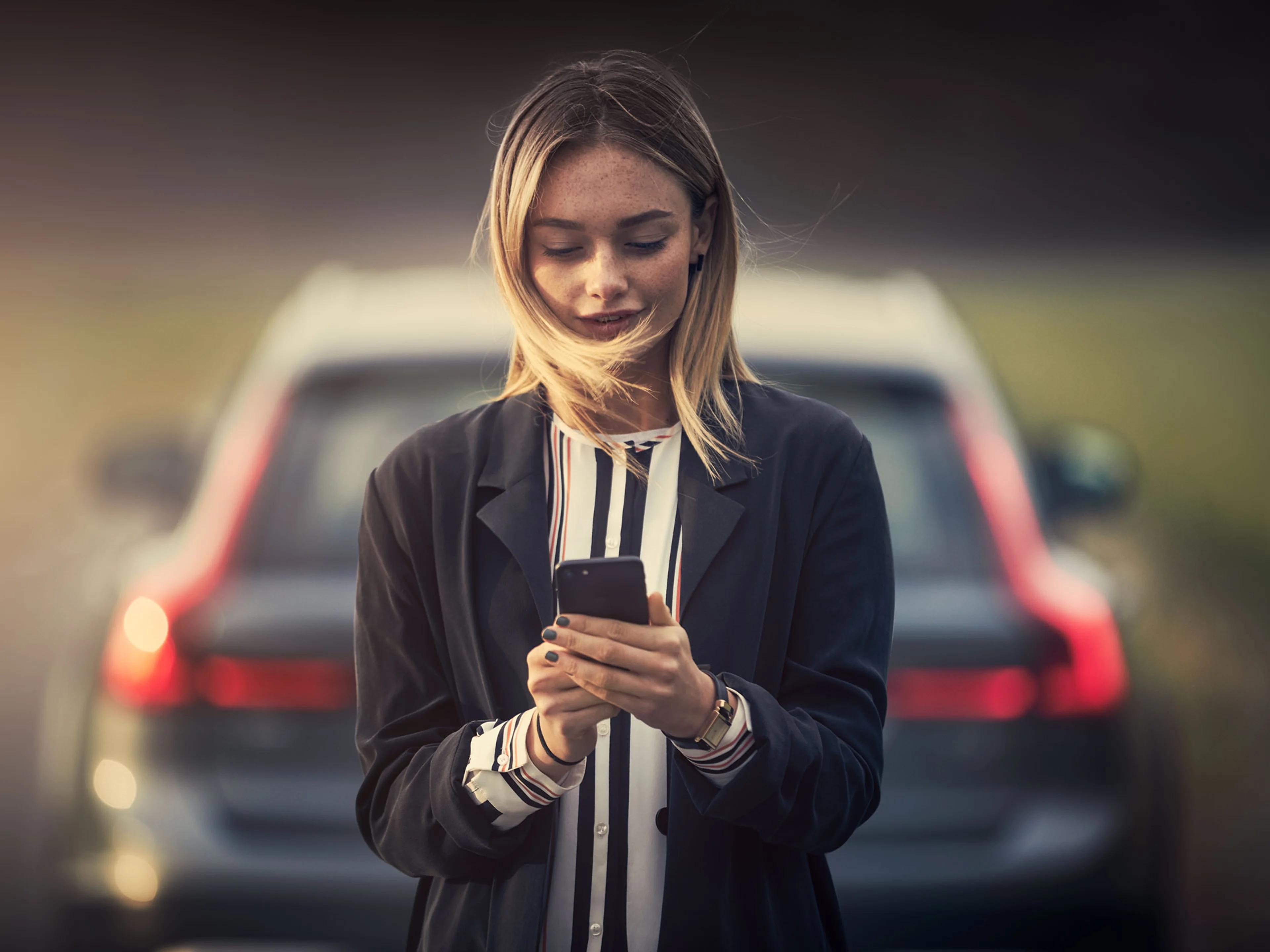 Una mujer con su teléfono en mano de espaldas a un Volvo XC60