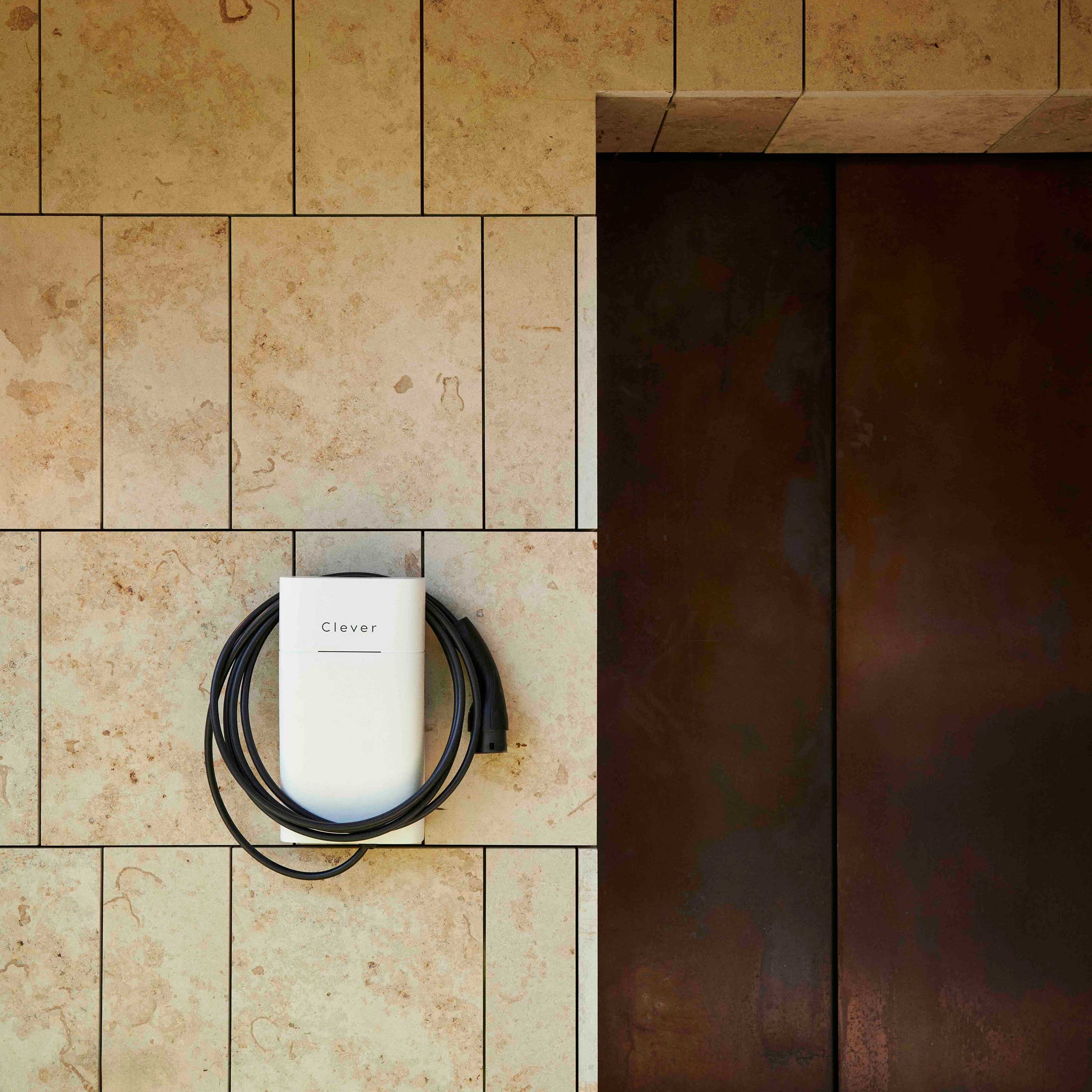 En elegant elbiloplader monteret på en beige flisevæg med et pænt oprullet sort kabel. Miljøet udstråler et moderne, minimalistisk design.