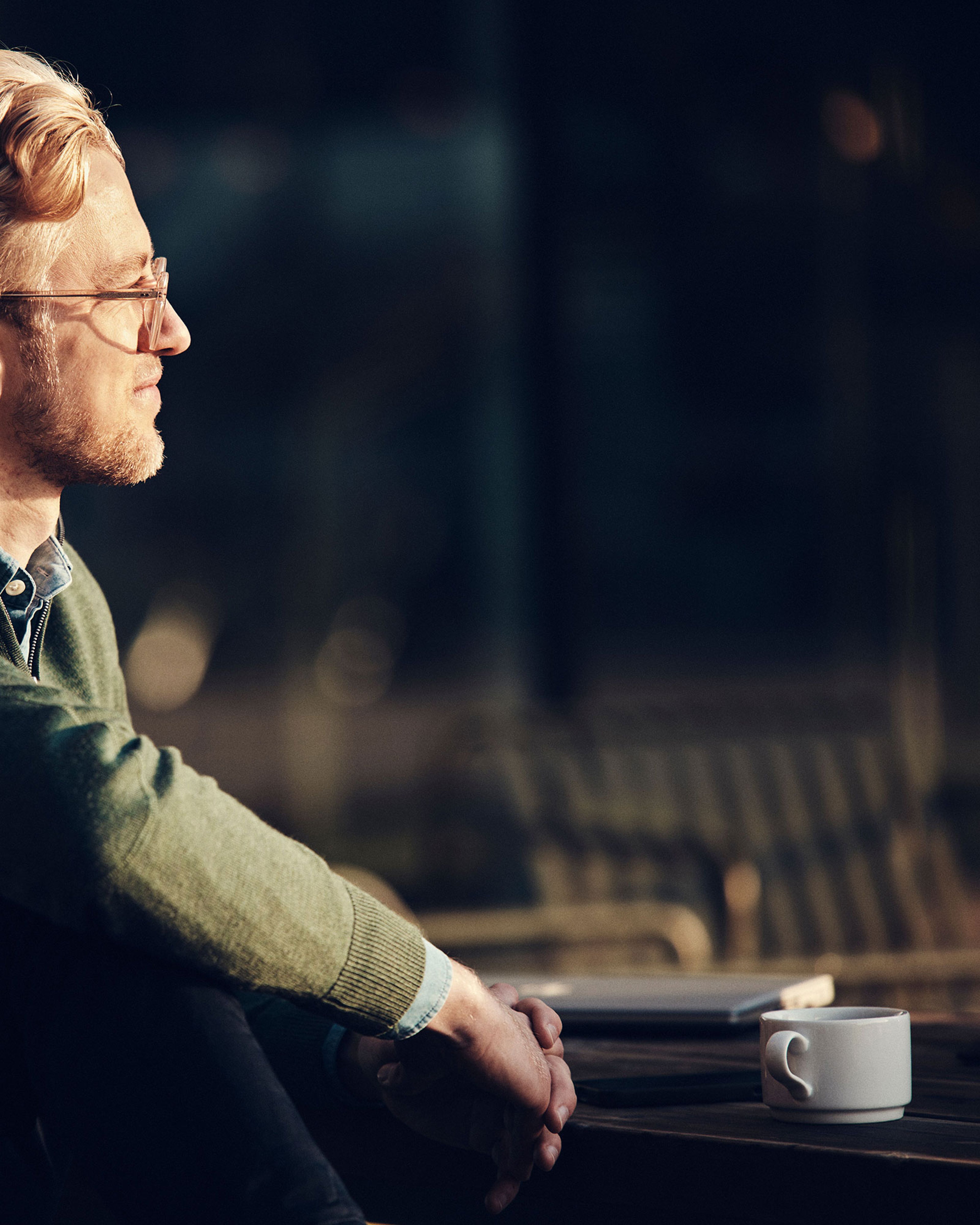 Een man met een bril en een groen vest zit aan een tafel en kijkt voorruit.