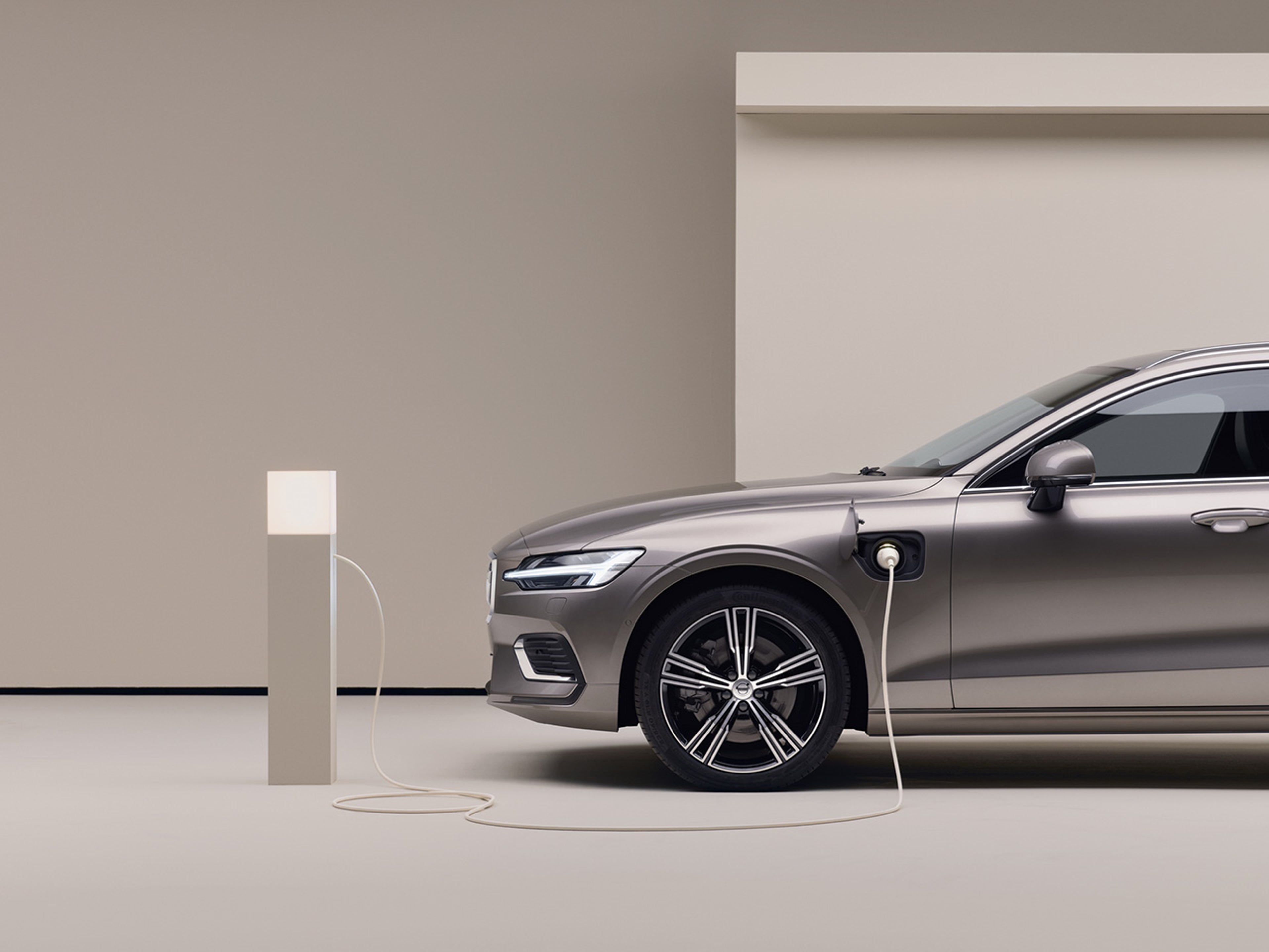 A side profile of the front half of the Volvo V60 plug-in hybrid. The car is plugged into an indoor charging station.