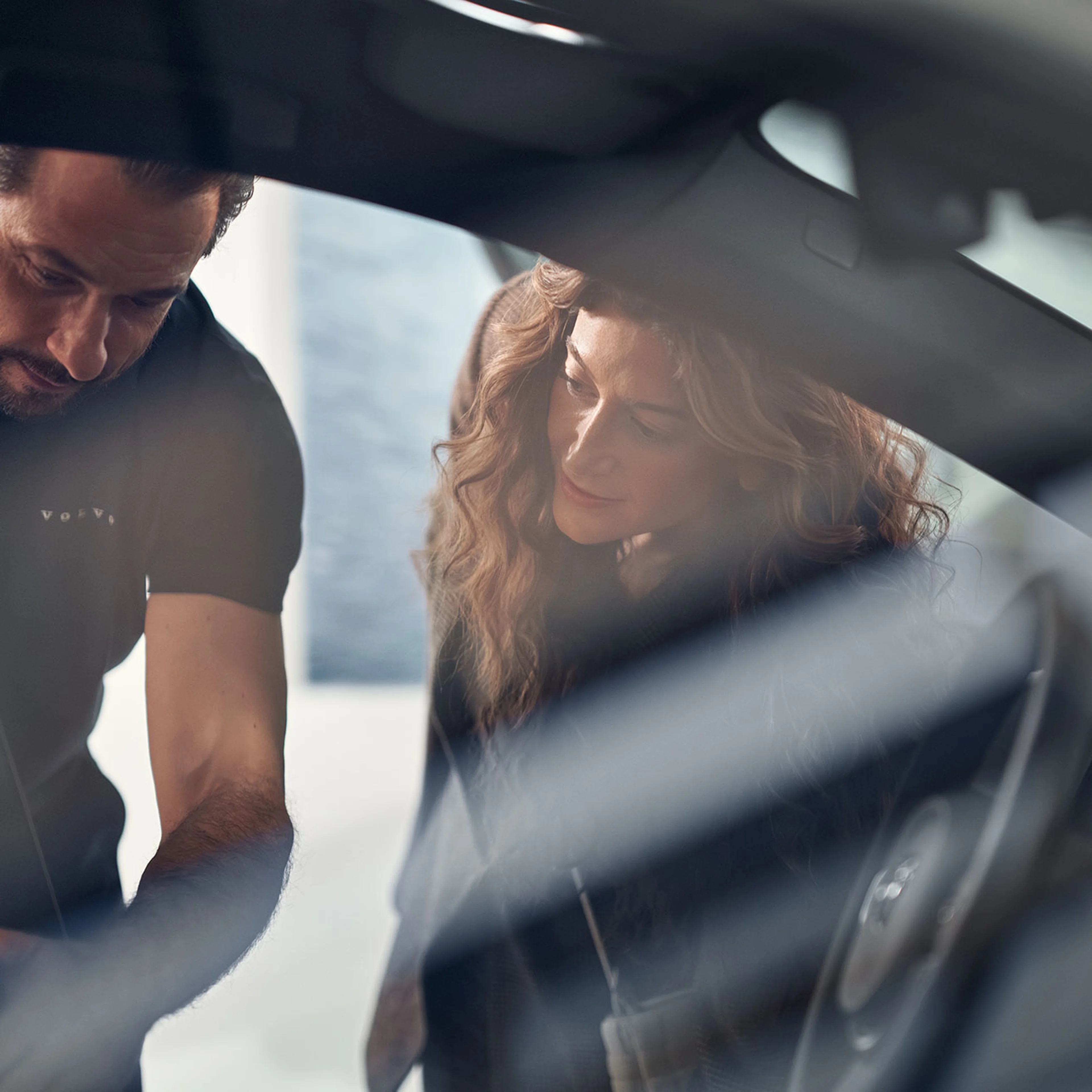 Set gennem passagerruden ser man en mand og en kvinde kigger ind i en bil fra Volvo gennem førersiden og manden forklarer kvinden om noget ved bilen.