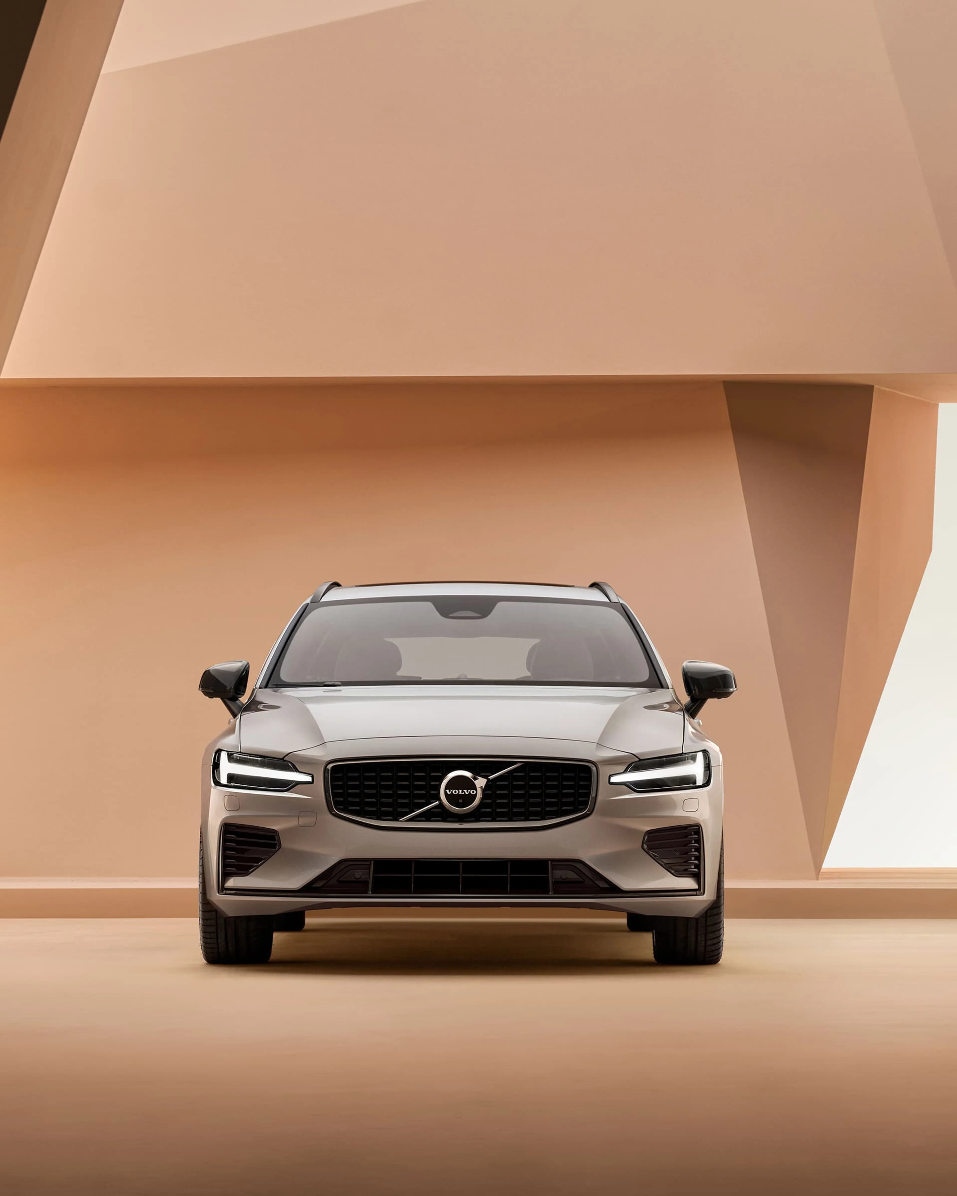 Une Volvo V60 grise en vue de face sur un fond de studio orange.