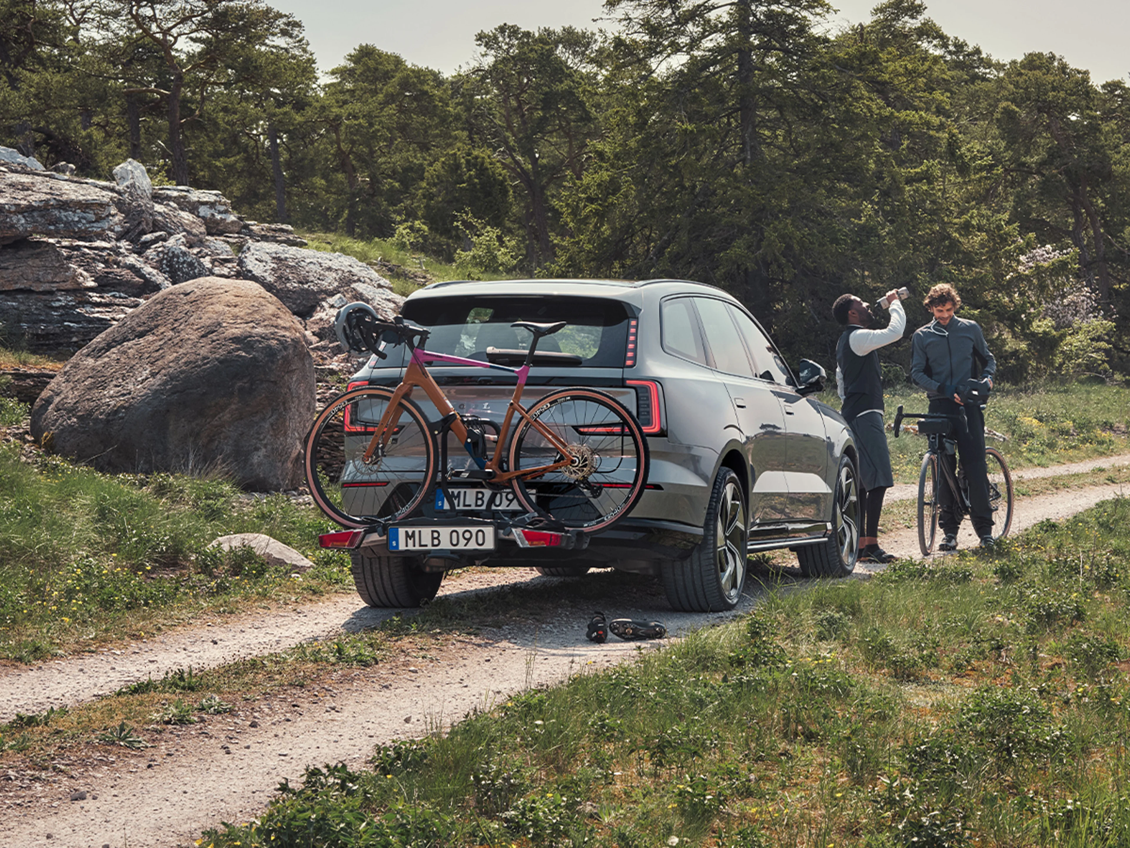 Två cyklister som står och pratar vid en Volvo EX30 med monterad cykelhållare på dragkroken med en cykel fäst