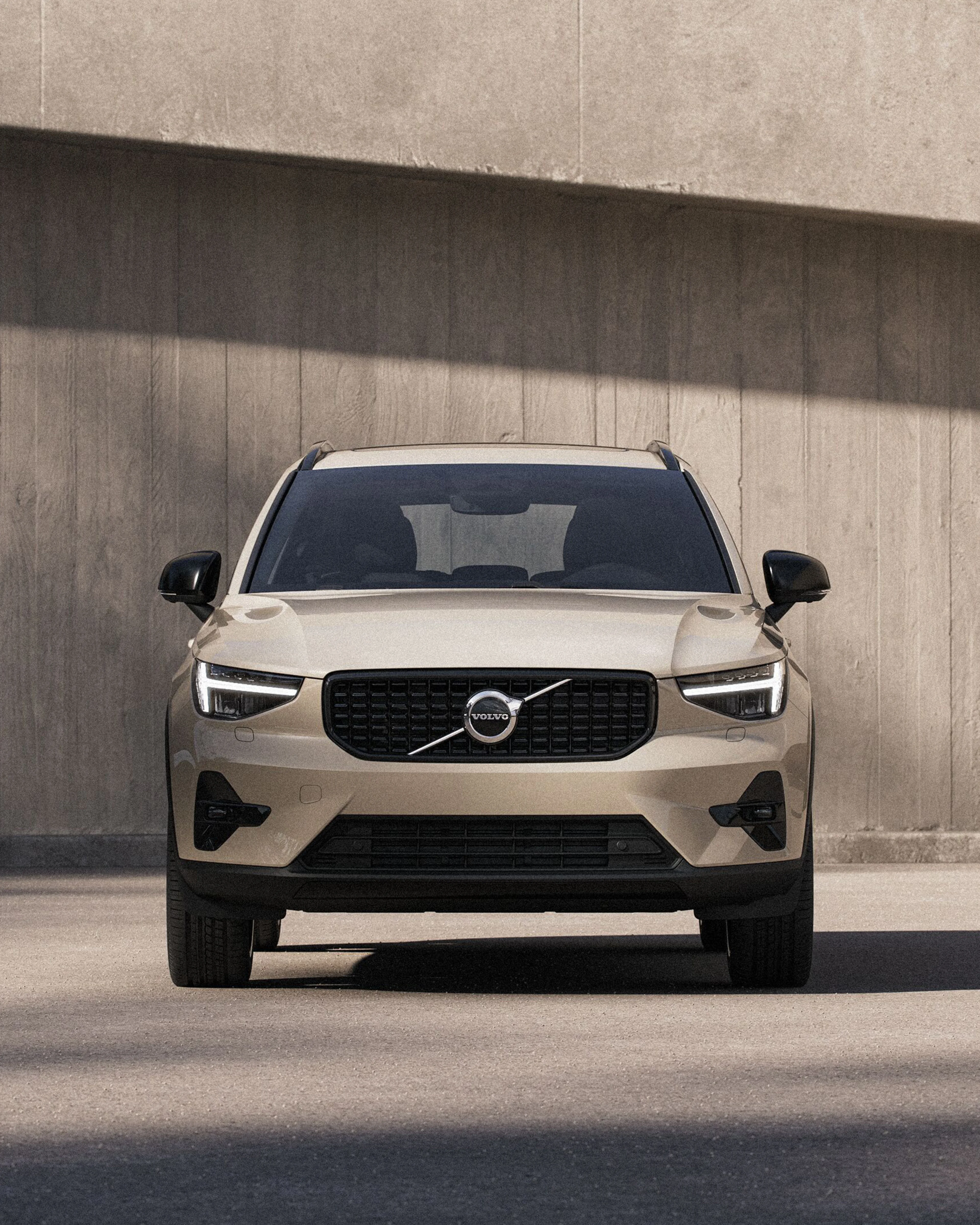 The front profile of a Navy XC90 on a pebble beach with a calm sea behind it