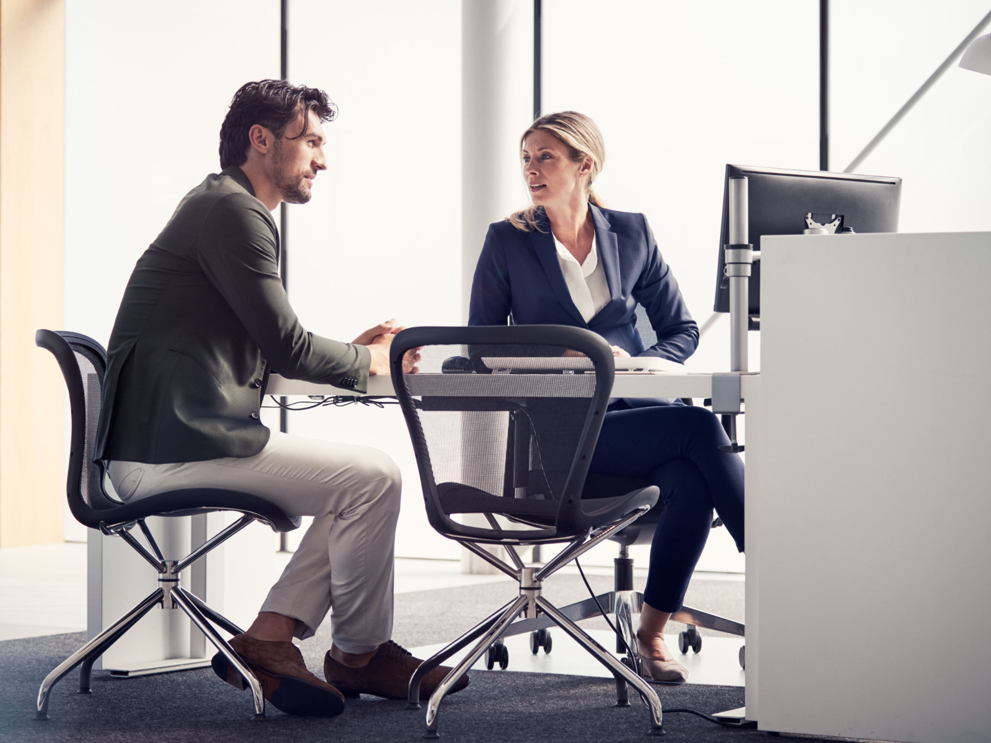 Ein Mann und eine Frau sitzen an einem Tisch mit einem Computer und unterhalten sich.