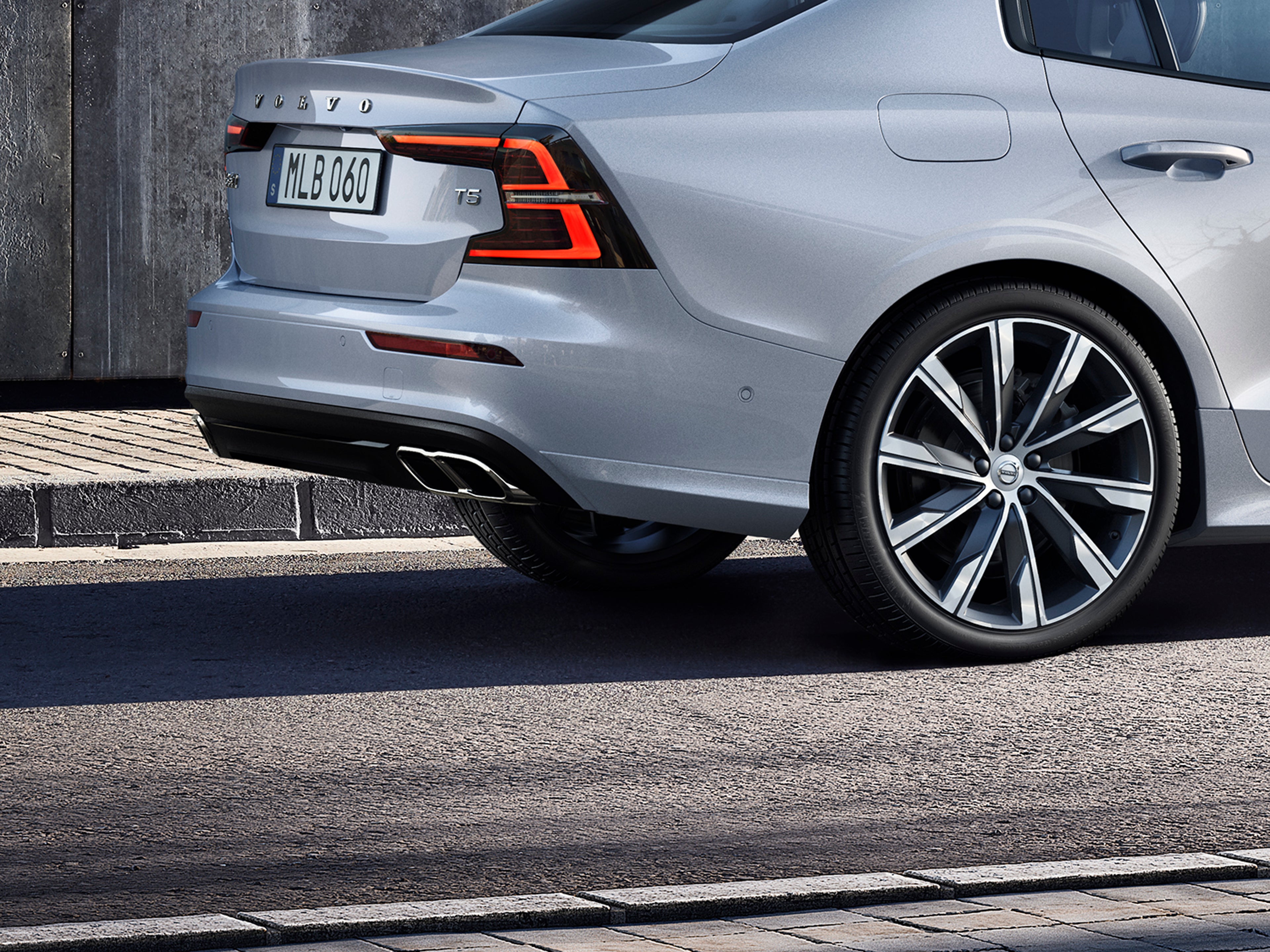 Vue arrière d’une Volvo grise avec plaque MLB 060, feux allumés et une roue visible.