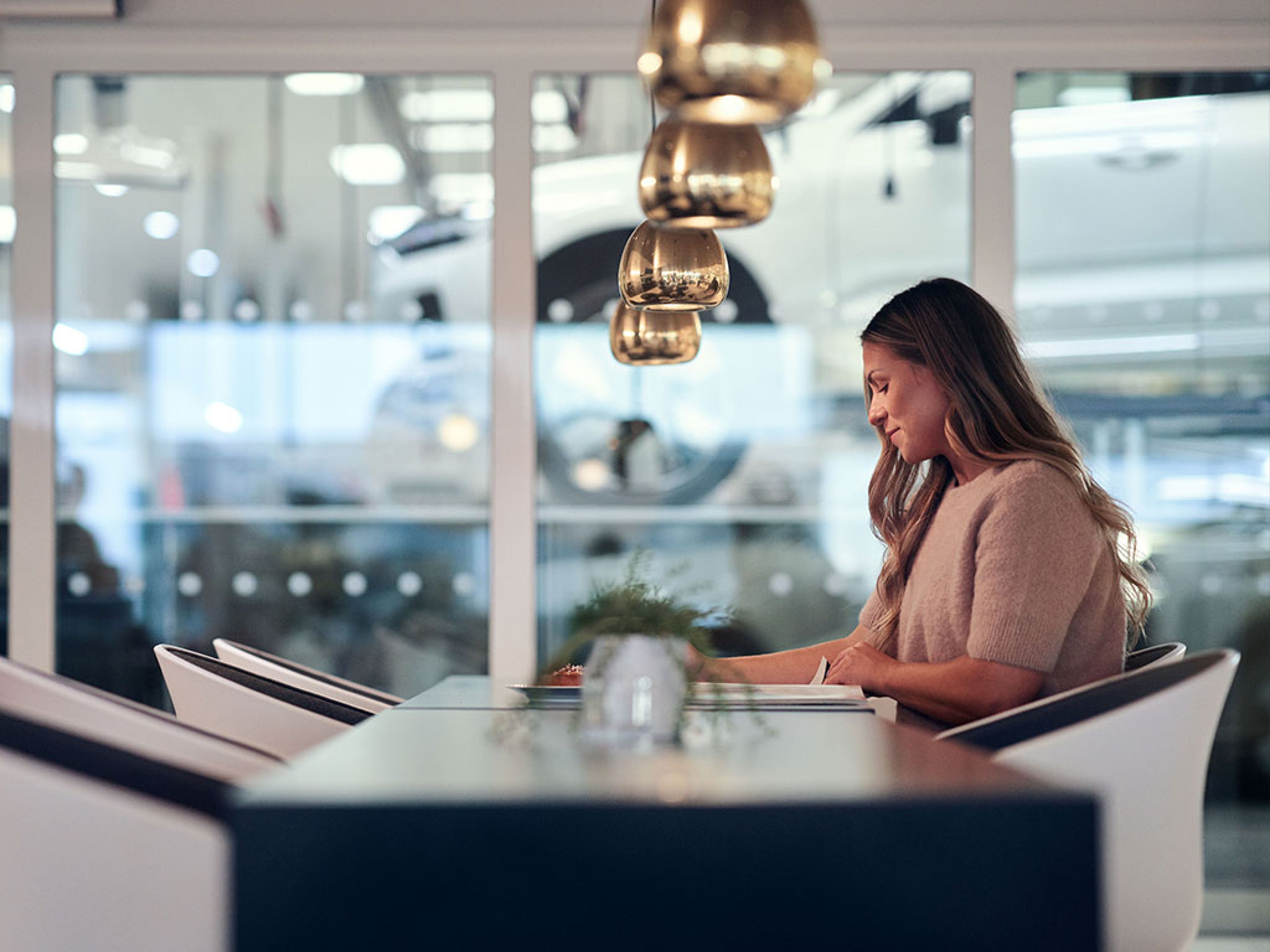 Femme assise à une table dans un bureau ou showroom moderne avec suspensions et murs en verre.