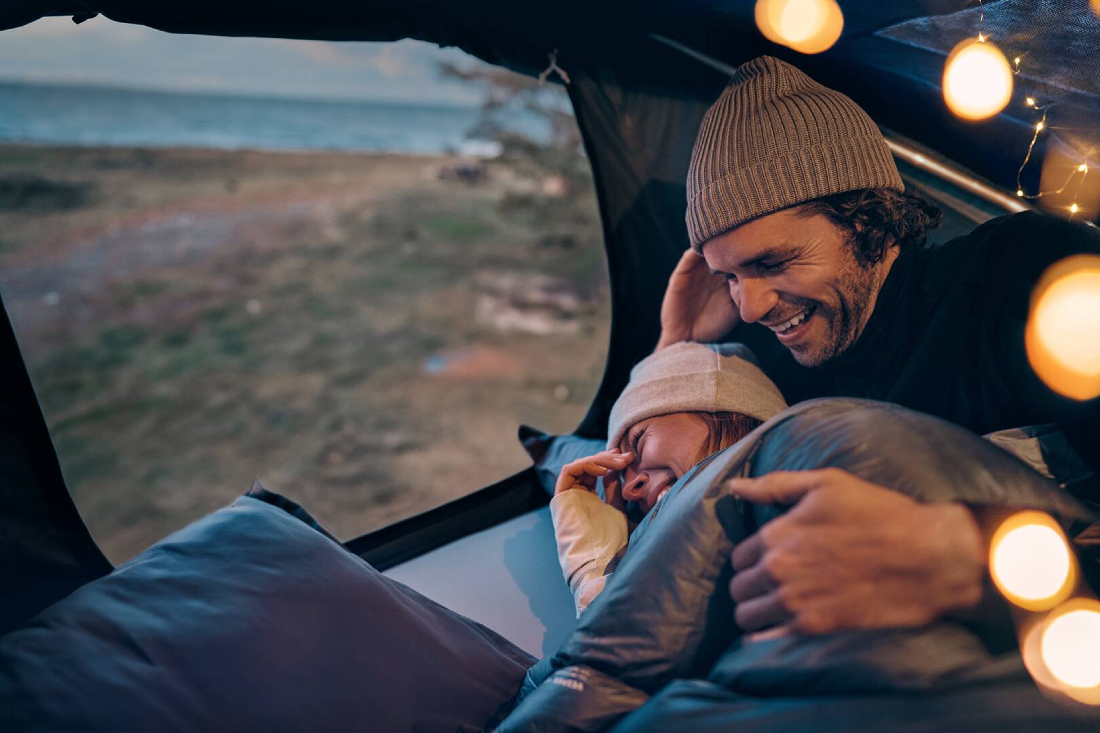 A cosy camp scene inside a Volvo roof tent overlooking a serene lake, warm lighting, and soft blankets create an inviting atmosphere.