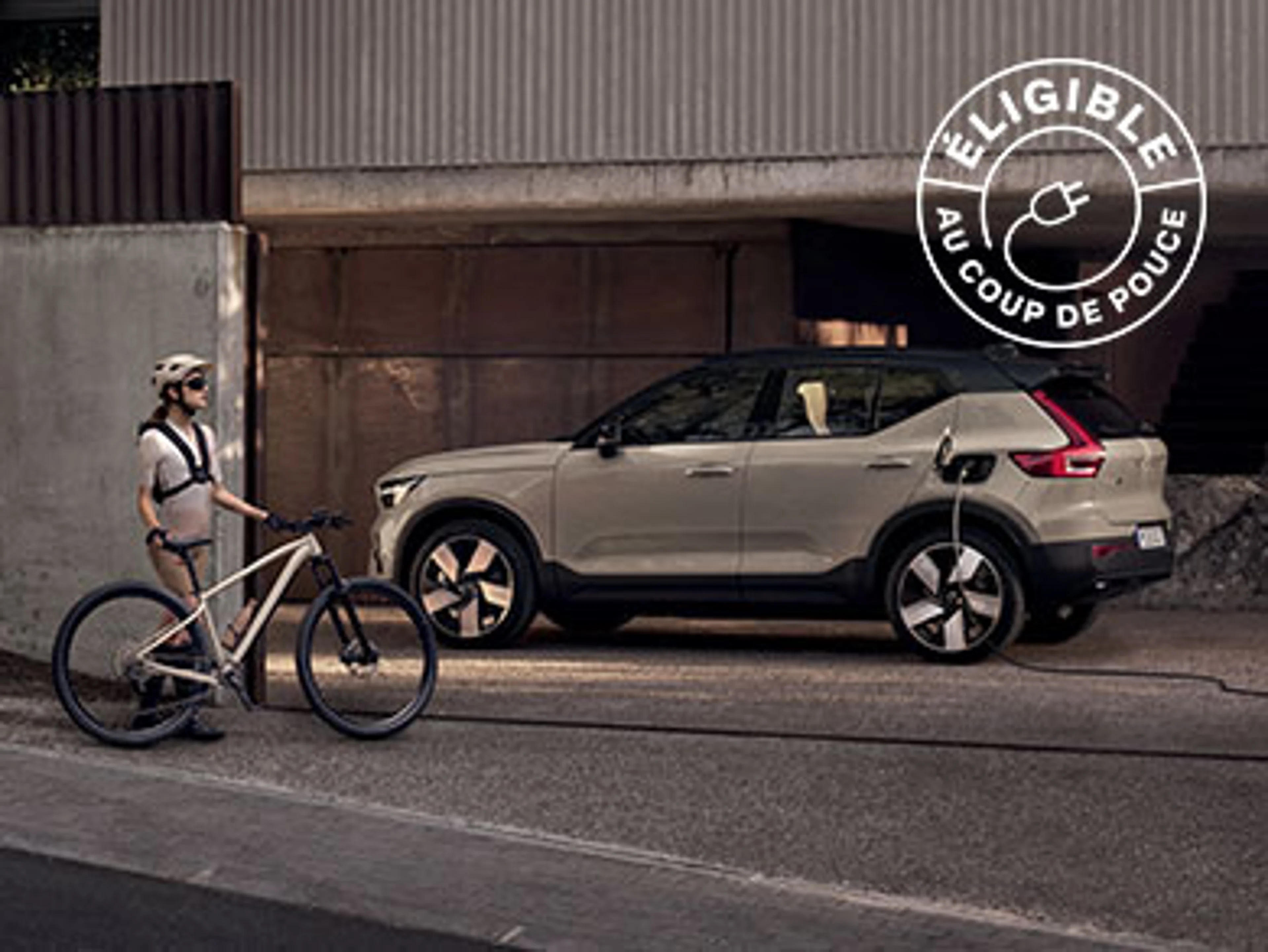 Femme avec vélo devant une Volvo EX40 électrique en charge dans une allée.