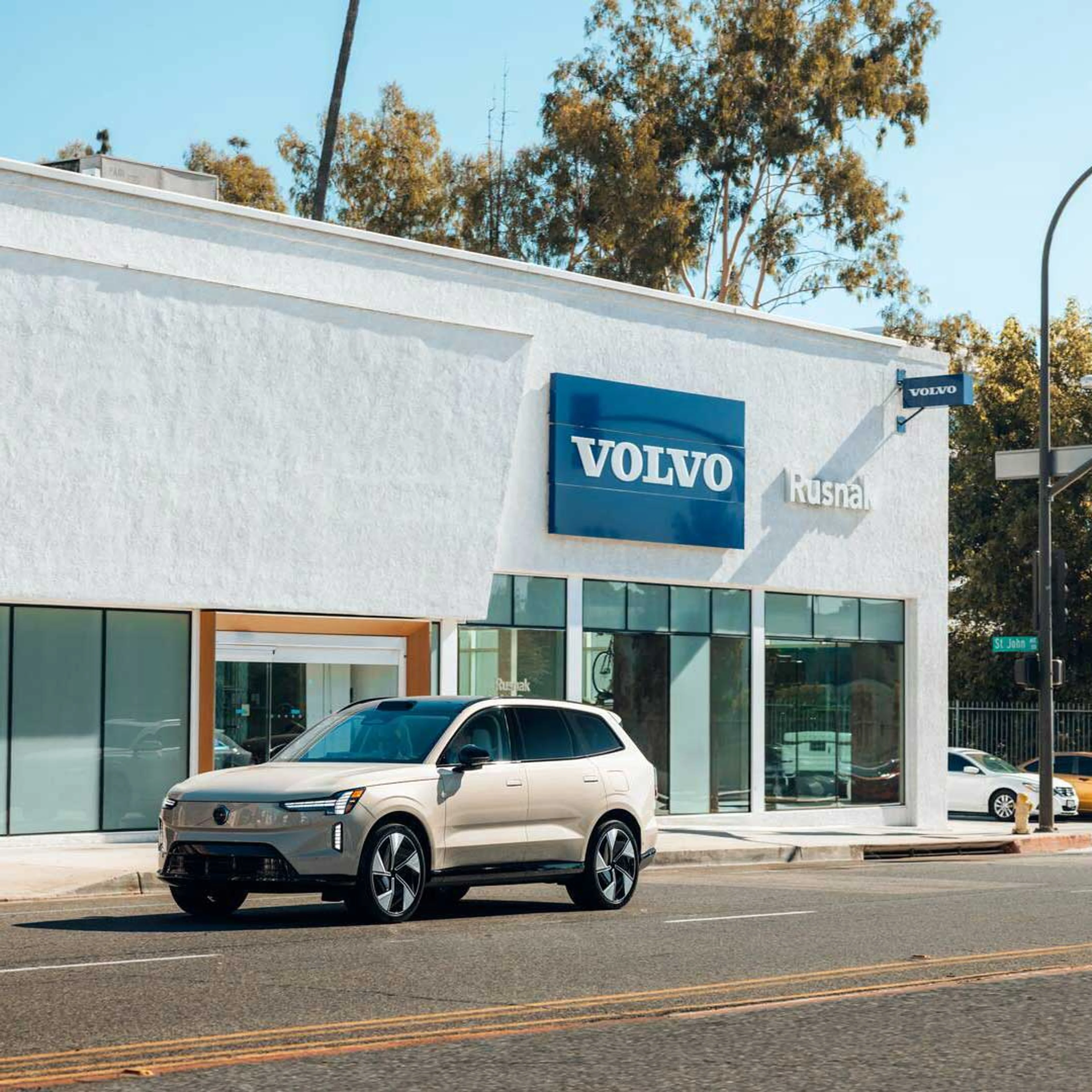 En stor elektrisk bil fra Volvo ses fra skråt fra siden, holdende foran et hvidt Volvo værksted i Los Angeles.