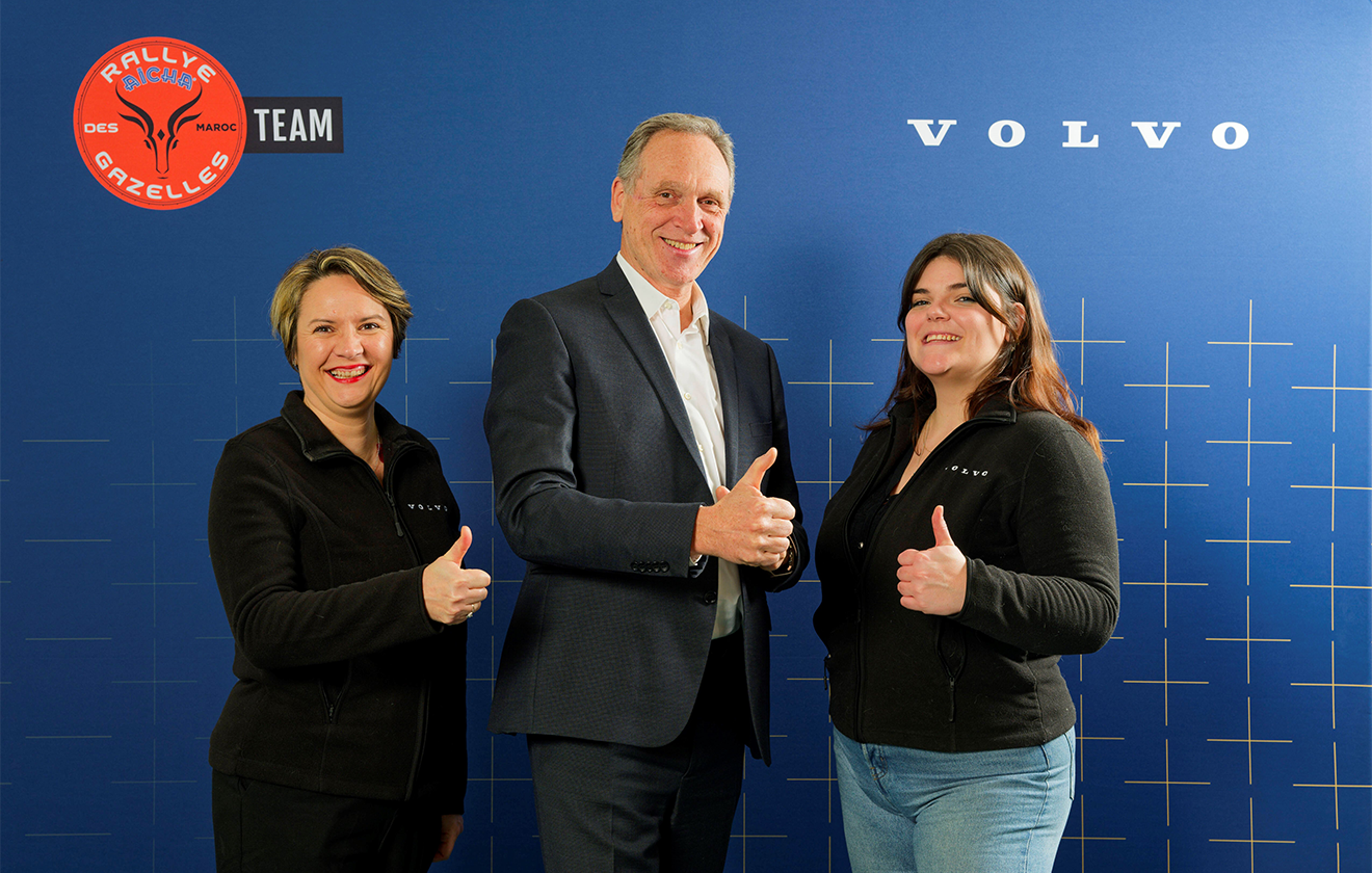 Yves Pasquier-Desvignes, Marie Brabant et Séverine Mary font un pouce levé devant un fond bleu avec les logos Volvo et Rallye Aïcha des Gazelles