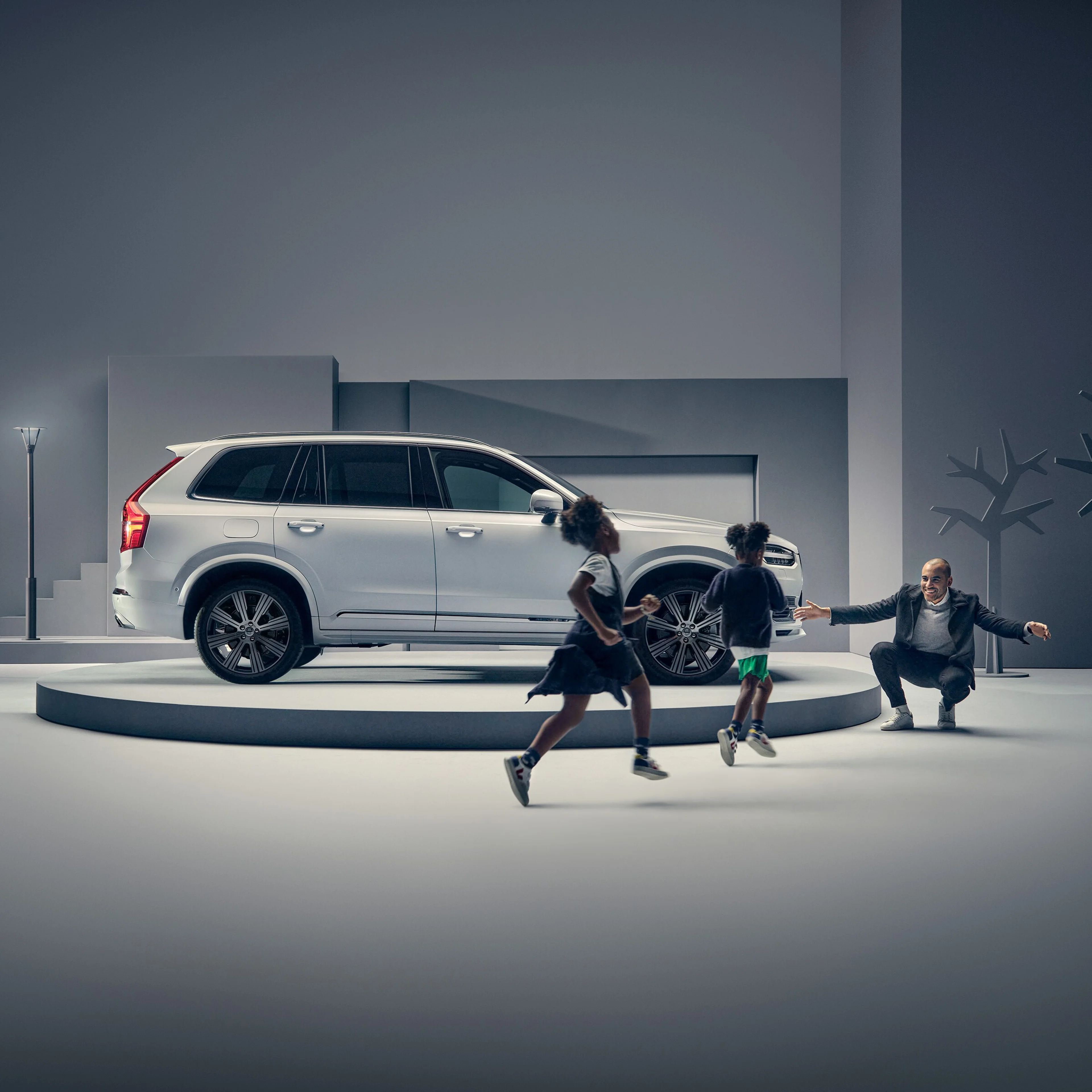 A man greets two children in front of a Volvo on a podium.