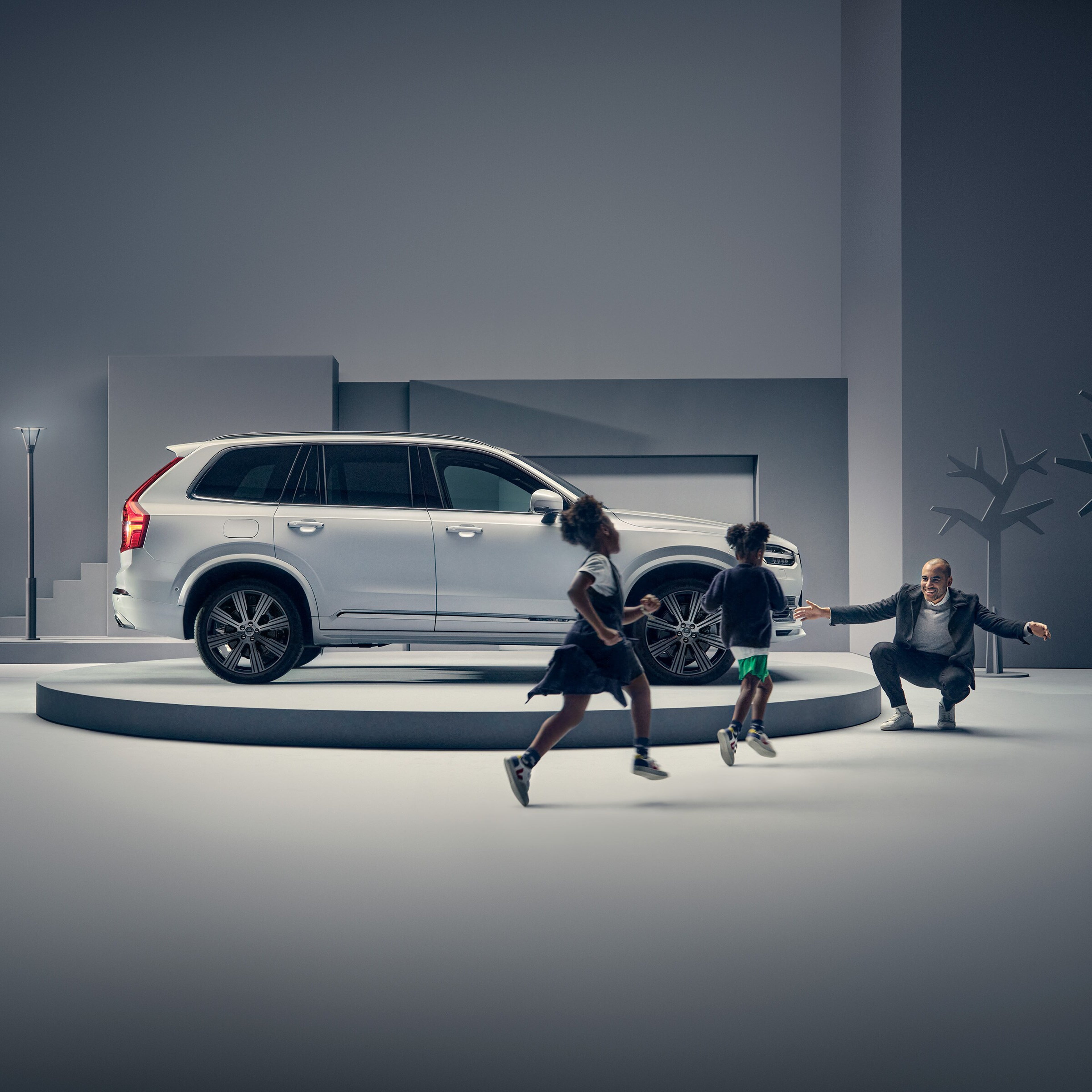 Podyumda Volvo'nun önünde iki çocuğu karşılayan bir adam.