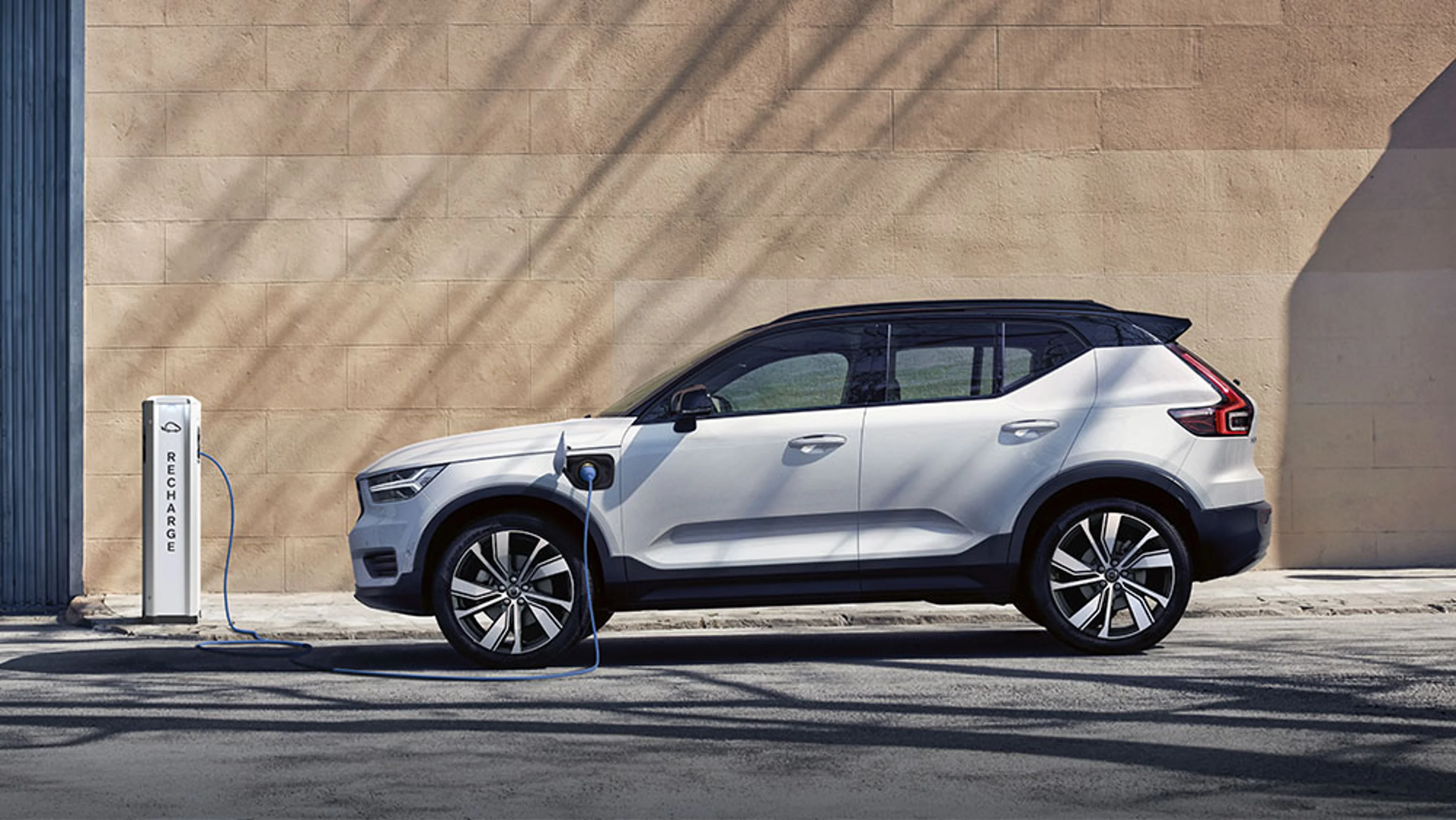 XC40 branchée à une borne de recharge avec câble bleu, stationnée devant un mur beige et une porte bleue