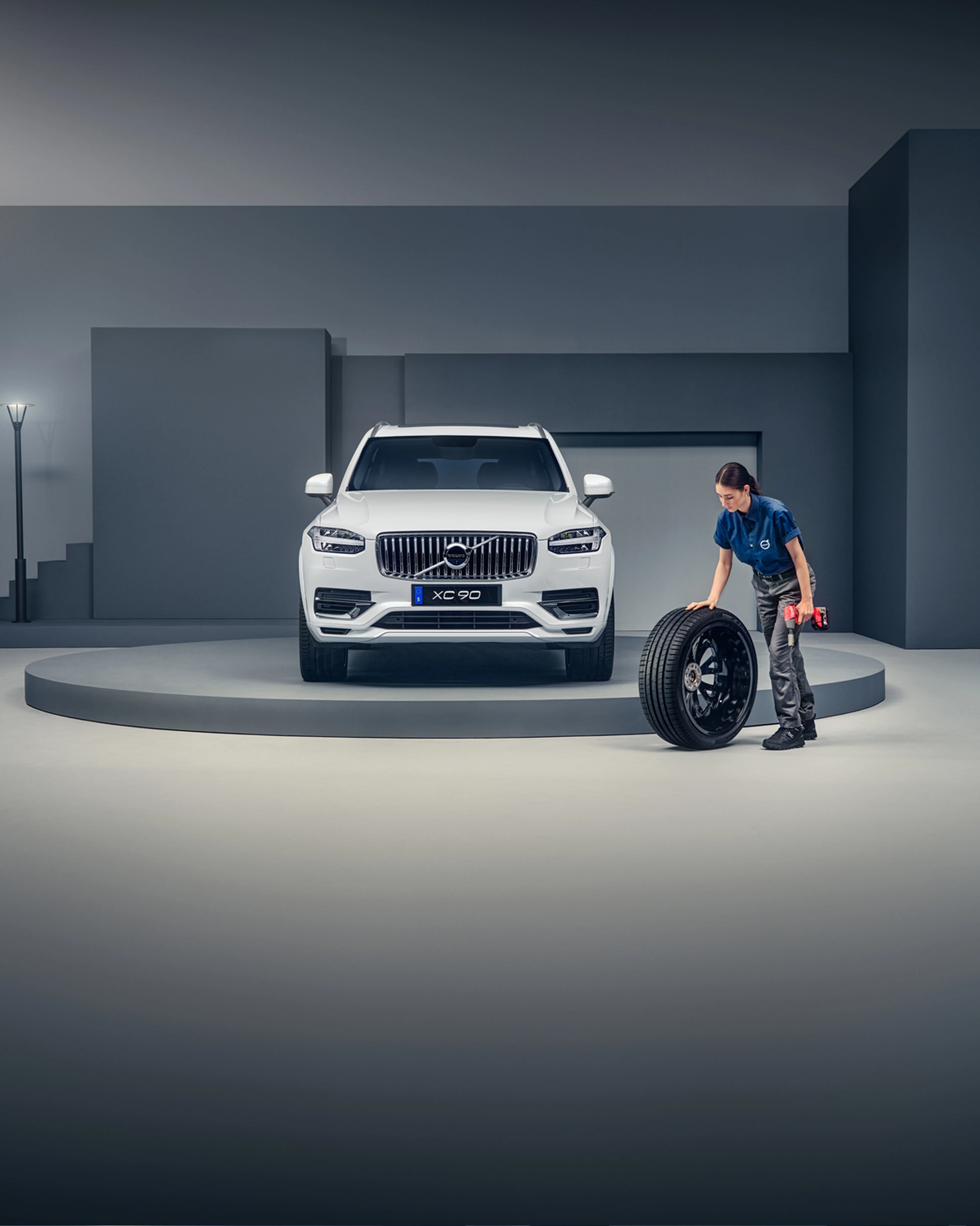 Kvinnelig Volvoansatt triller ett hjul i forbindelse med hjulskift av en hvit XC90