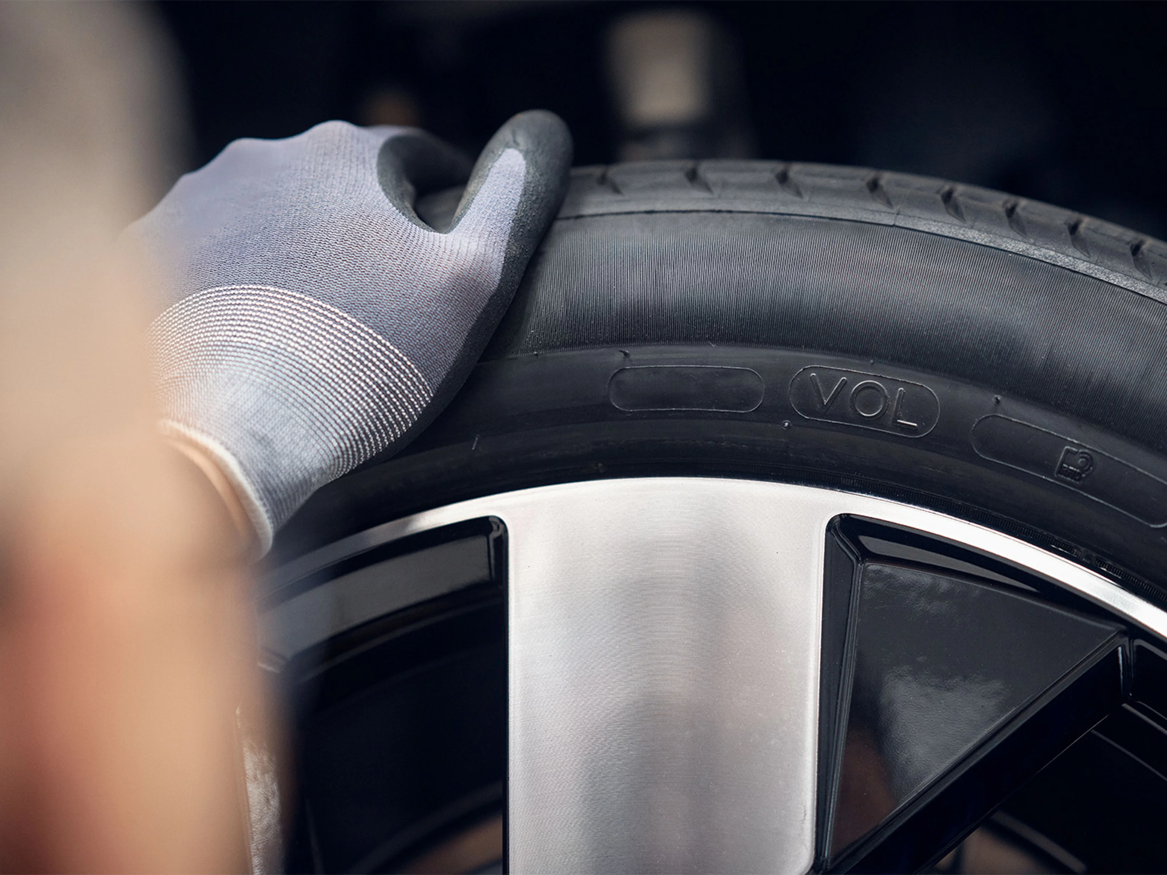 Close-up of a gloved hand inspecting a car tire, focusing on the tread and rim detail, highlighting Volvo automotive maintenance.