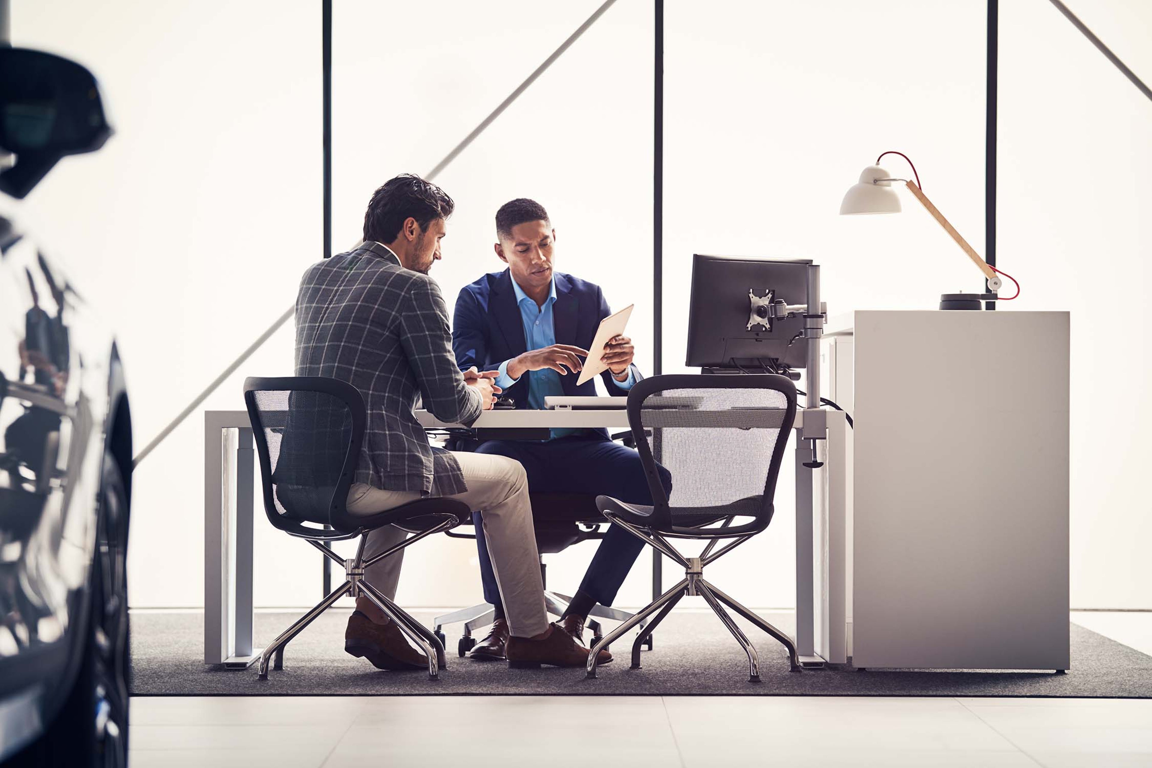 Dvoje muškaraca razgovaraju za stolom u modernom autosalonu