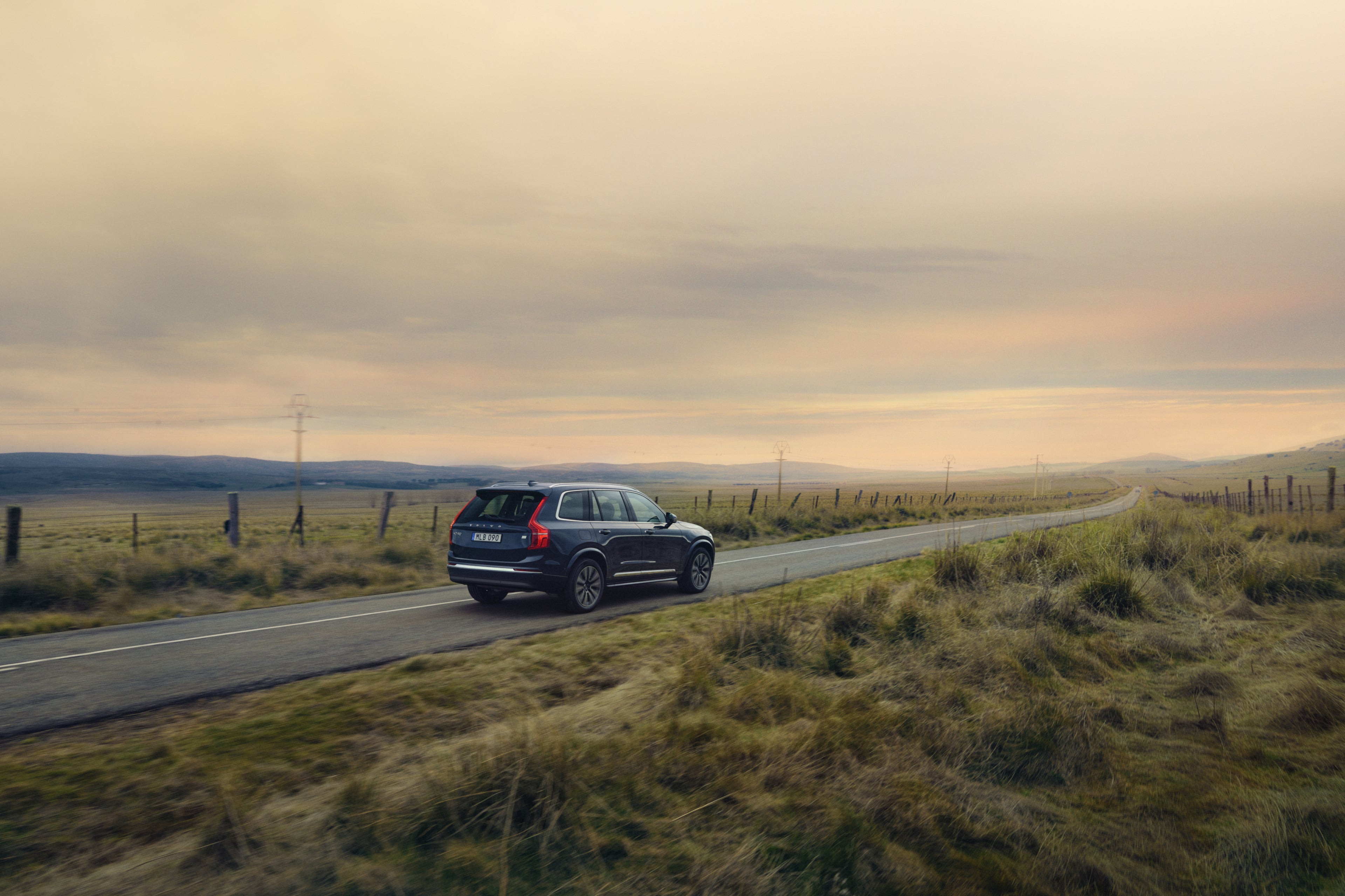 Volvo XC60 driving along empty winding road though grassy countryside in the twilight