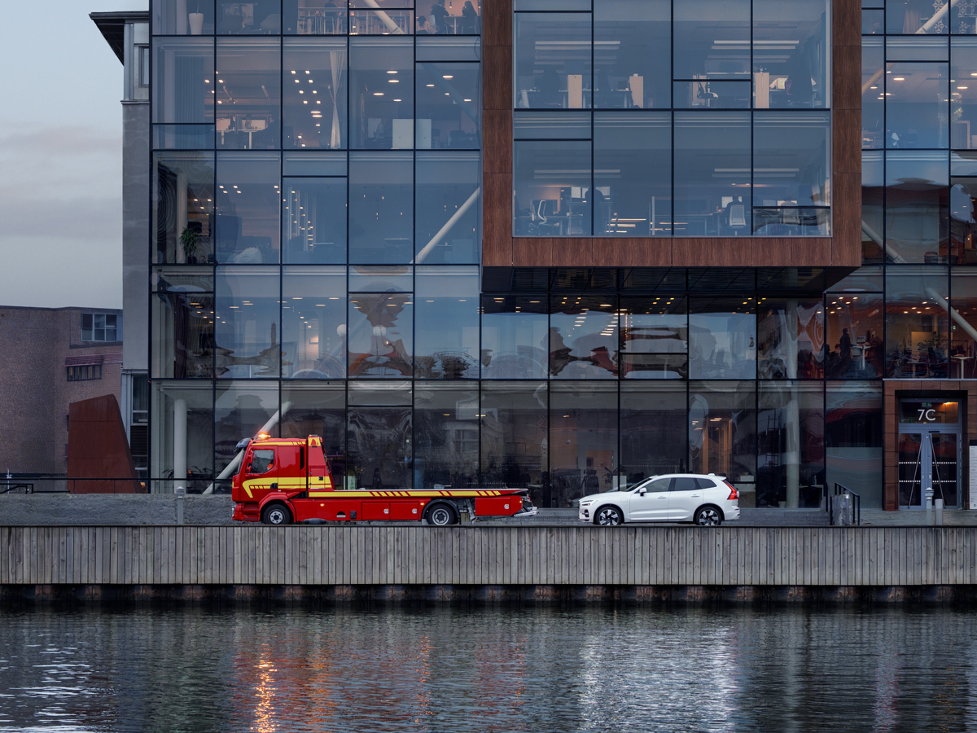 Bärgningsbil och bil framför glasbyggnad