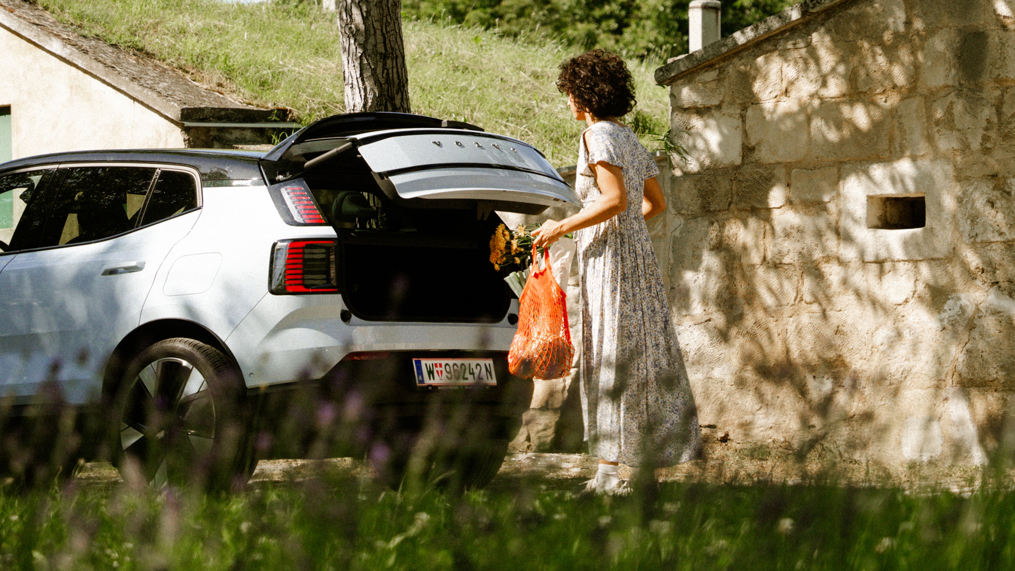 Eine Frau im Kleid steht am Kofferraum eines weißen Volvo EX30.