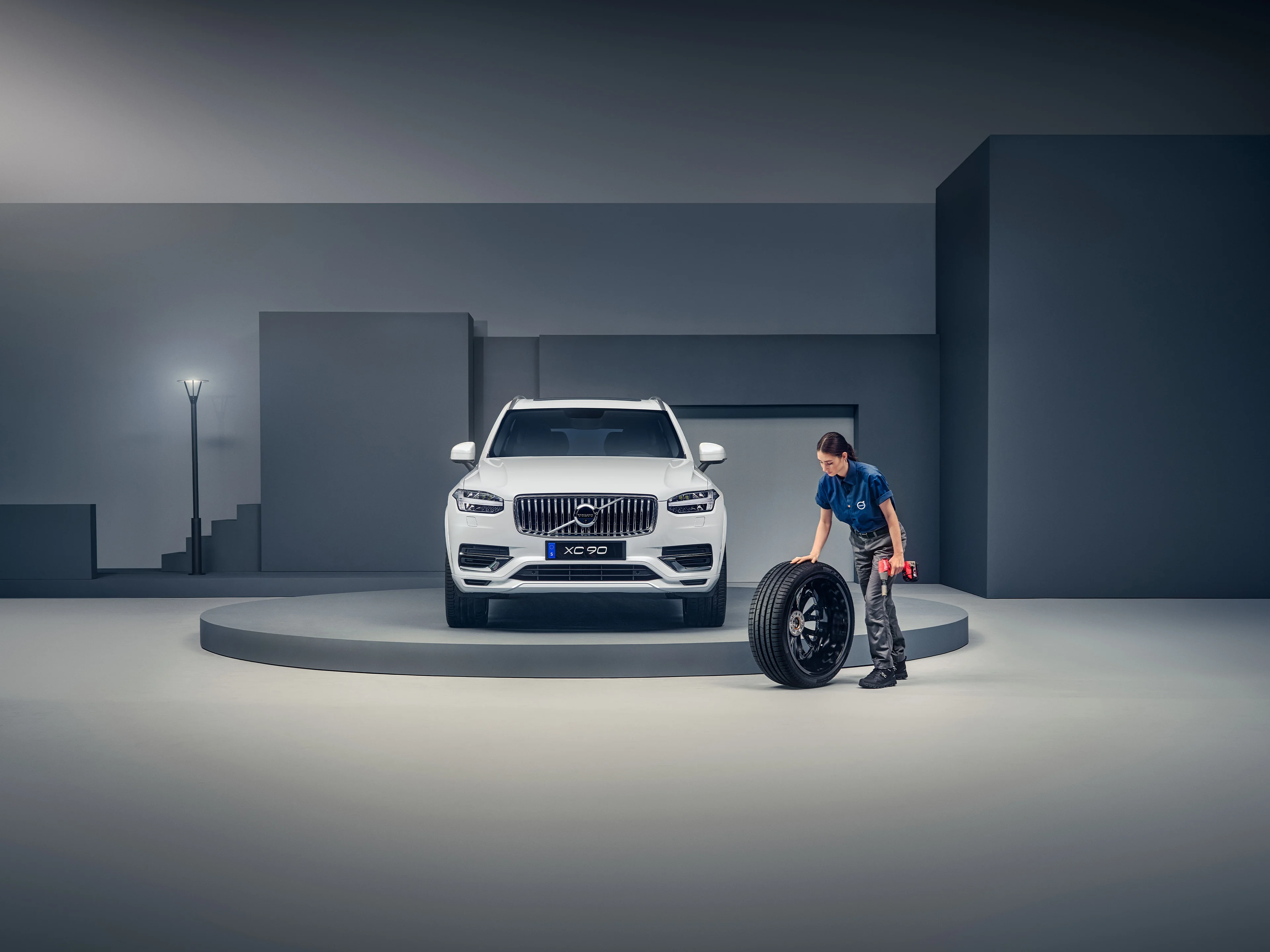 Mitarbeiterin rollt vor dem Volvo XC90 einen Reifen nach dem Wechseln weg.